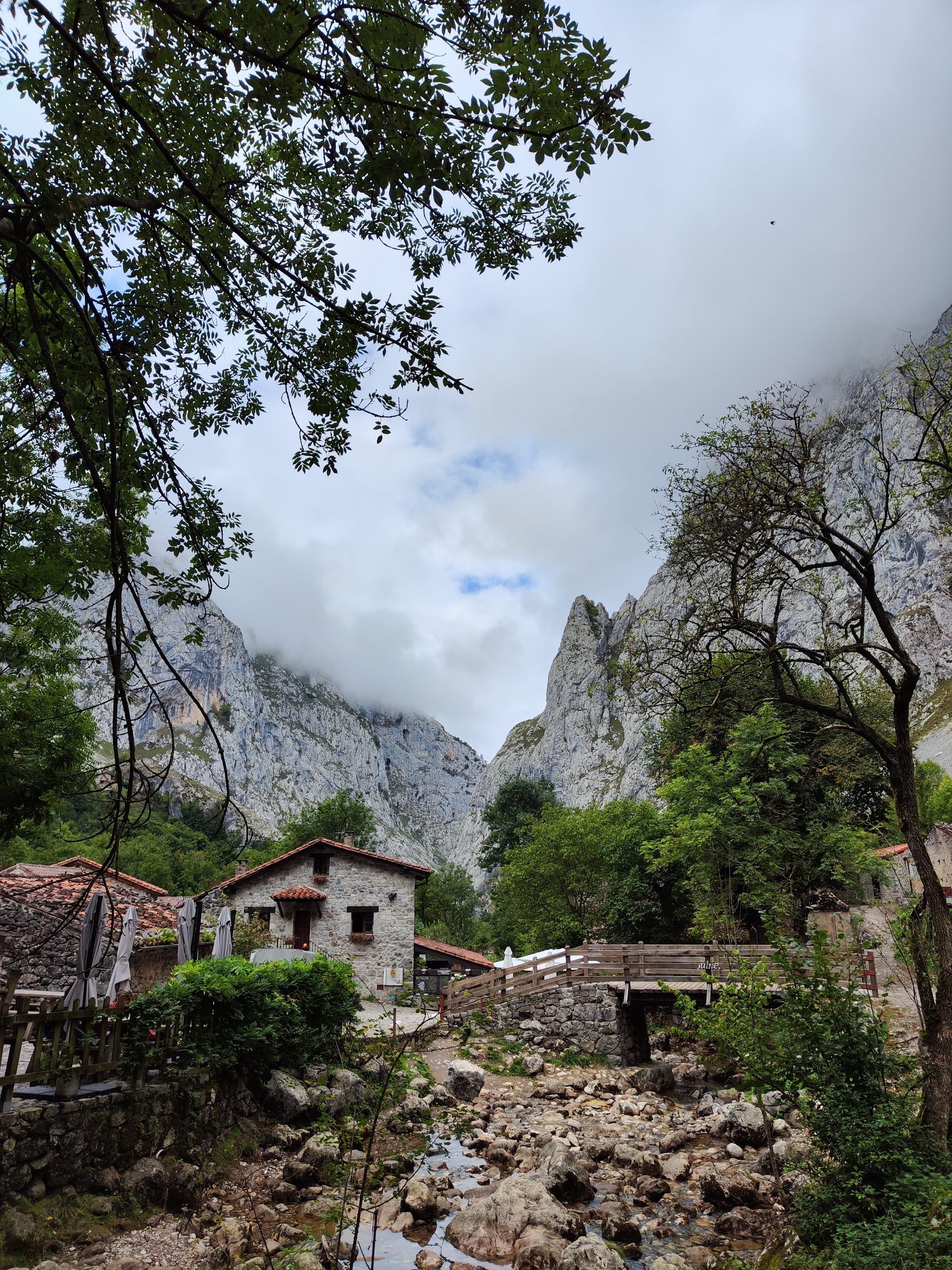 Pueblo de montaña con casas de piedra rodeado de imponentes cumbres rocosas y nubes.
