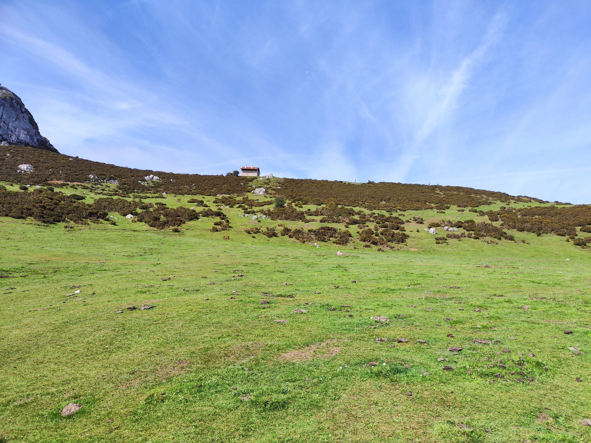 Pradera verde y colina con una pequeña cabaña de montaña bajo el cielo azul.
