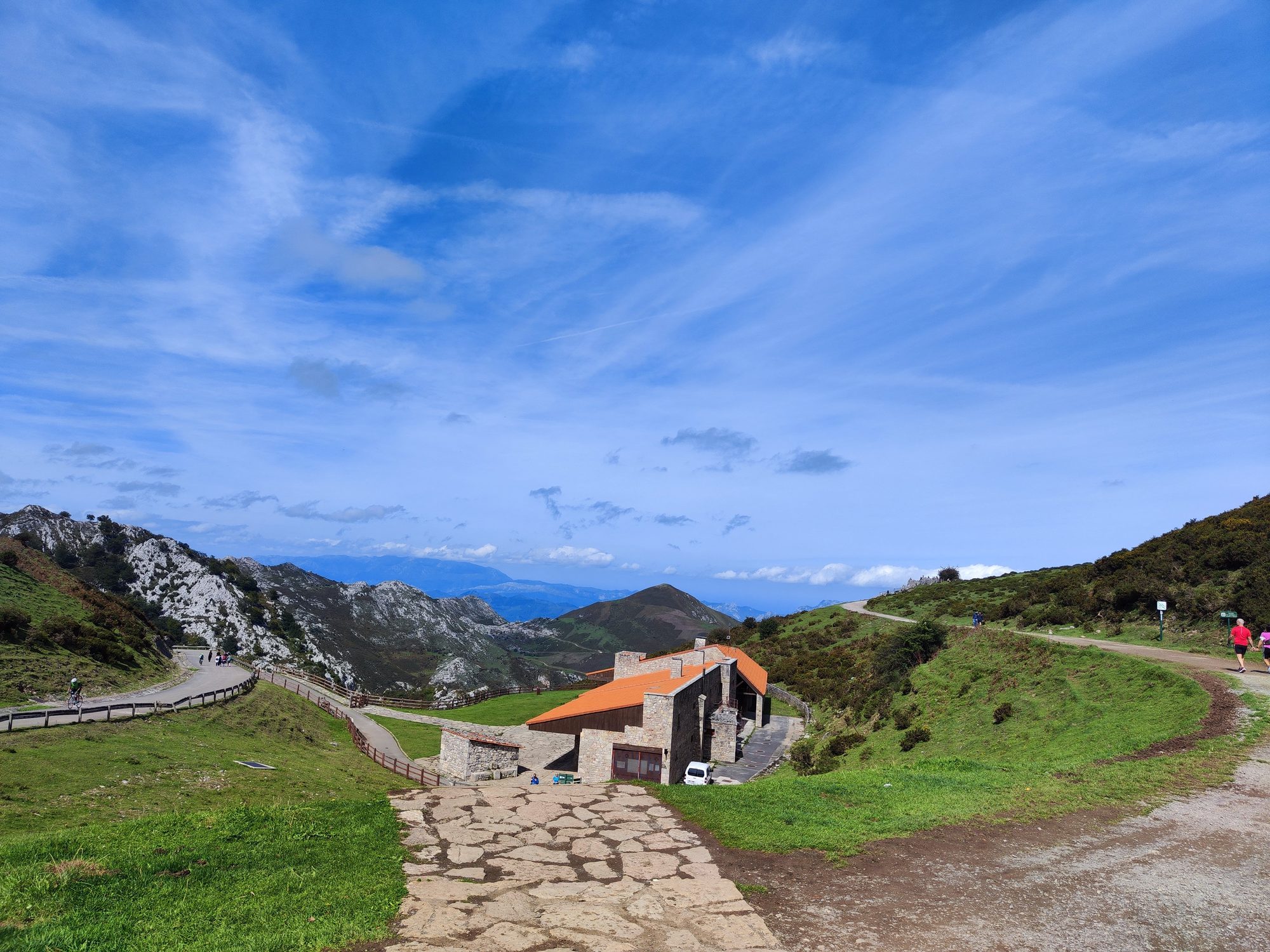 Edificio de piedra entre prados verdes y montañas escarpadas bajo un cielo azul despejado.