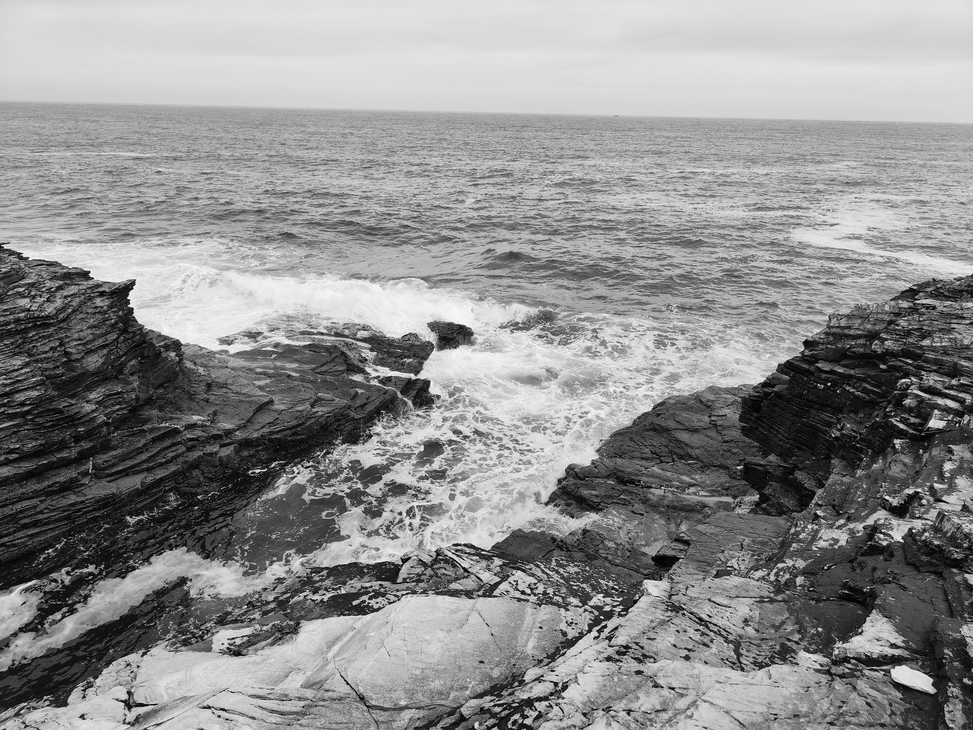Olas del mar Cantábrico rompiendo con fuerza entre acantilados rocosos en blanco y negro.