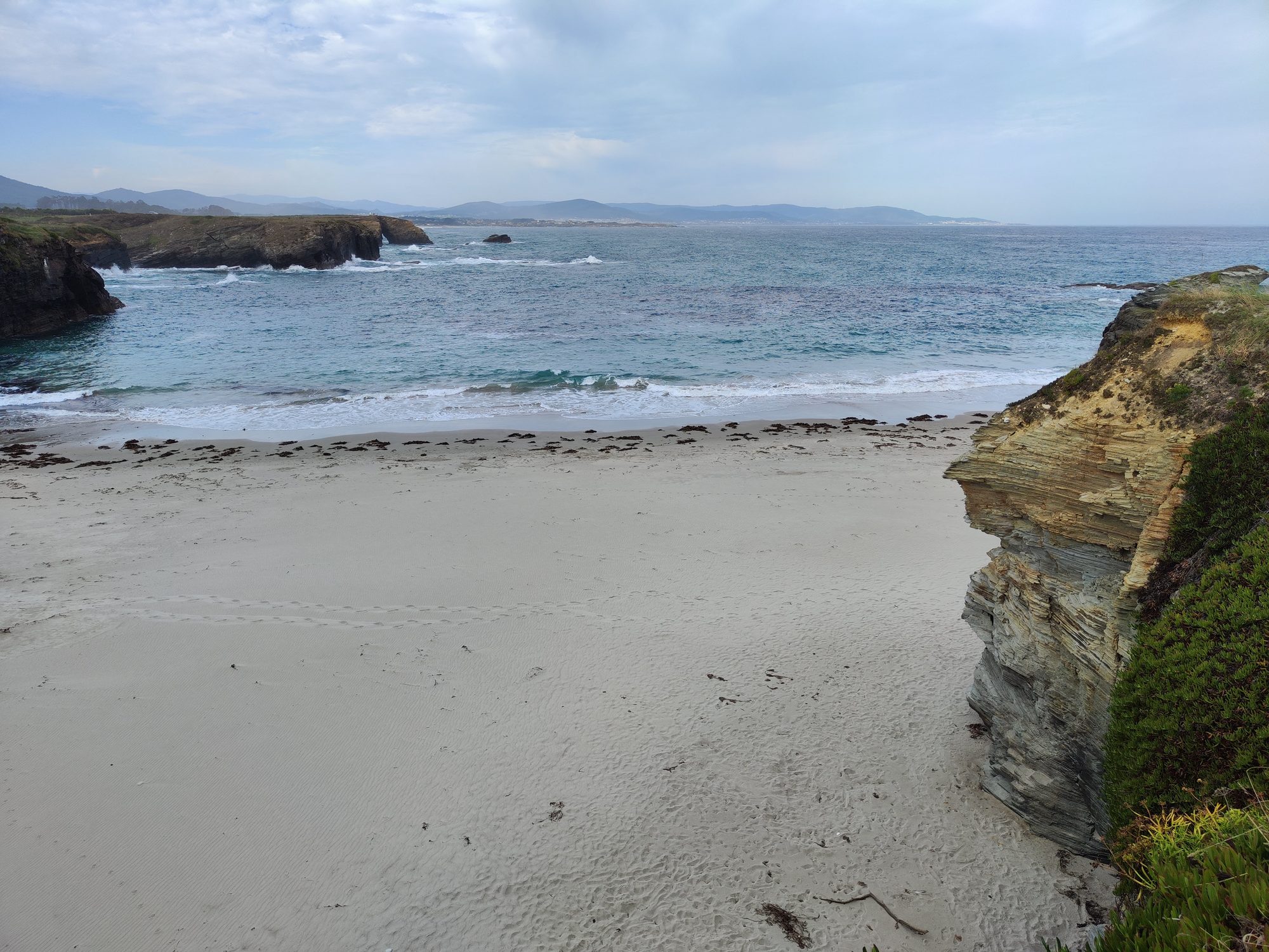 Playa de arena blanca rodeada de acantilados rocosos y mar Cantábrico en Ribadeo.