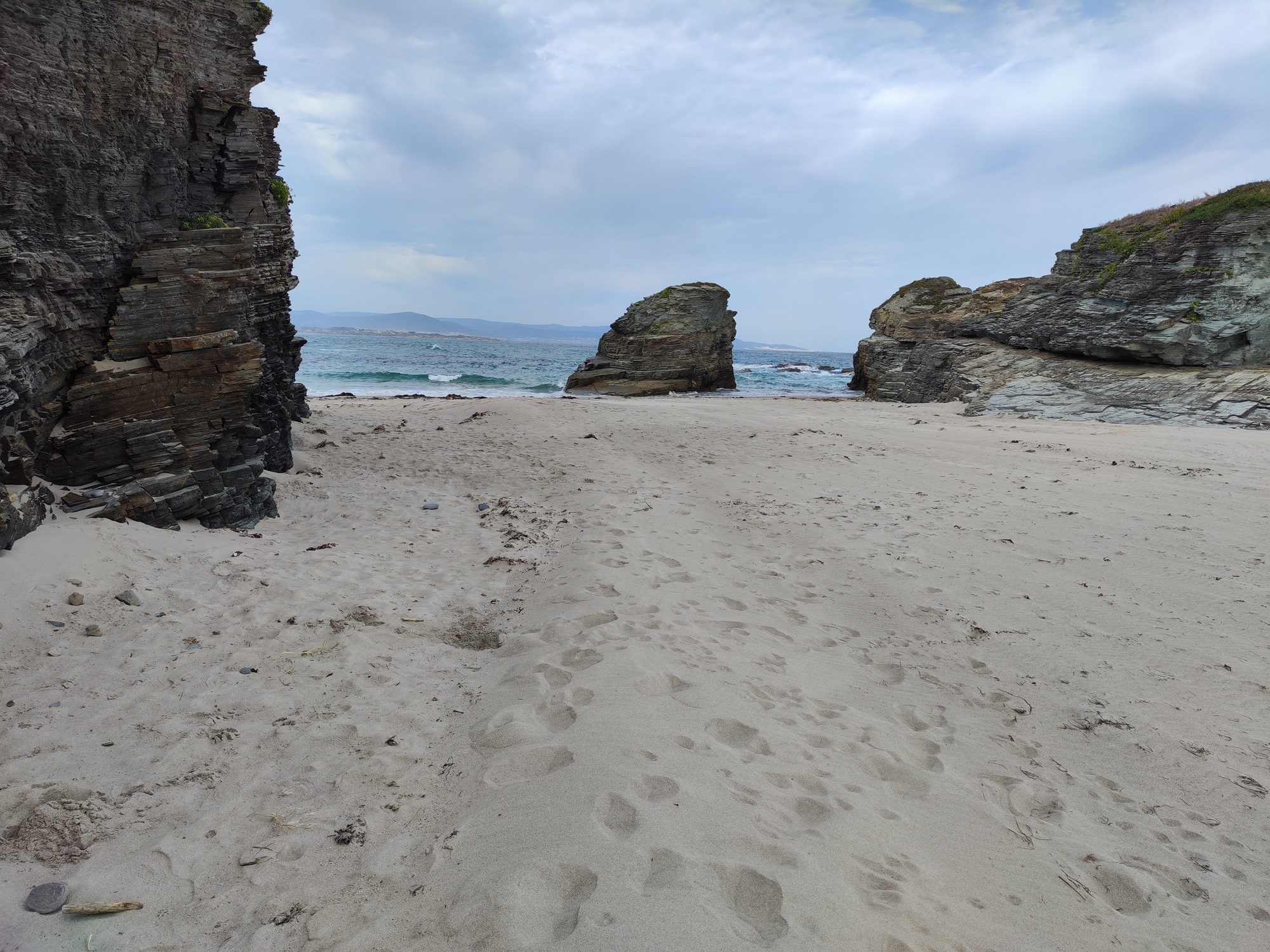 Playa de arena blanca rodeada de acantilados rocosos junto al mar Cantábrico.