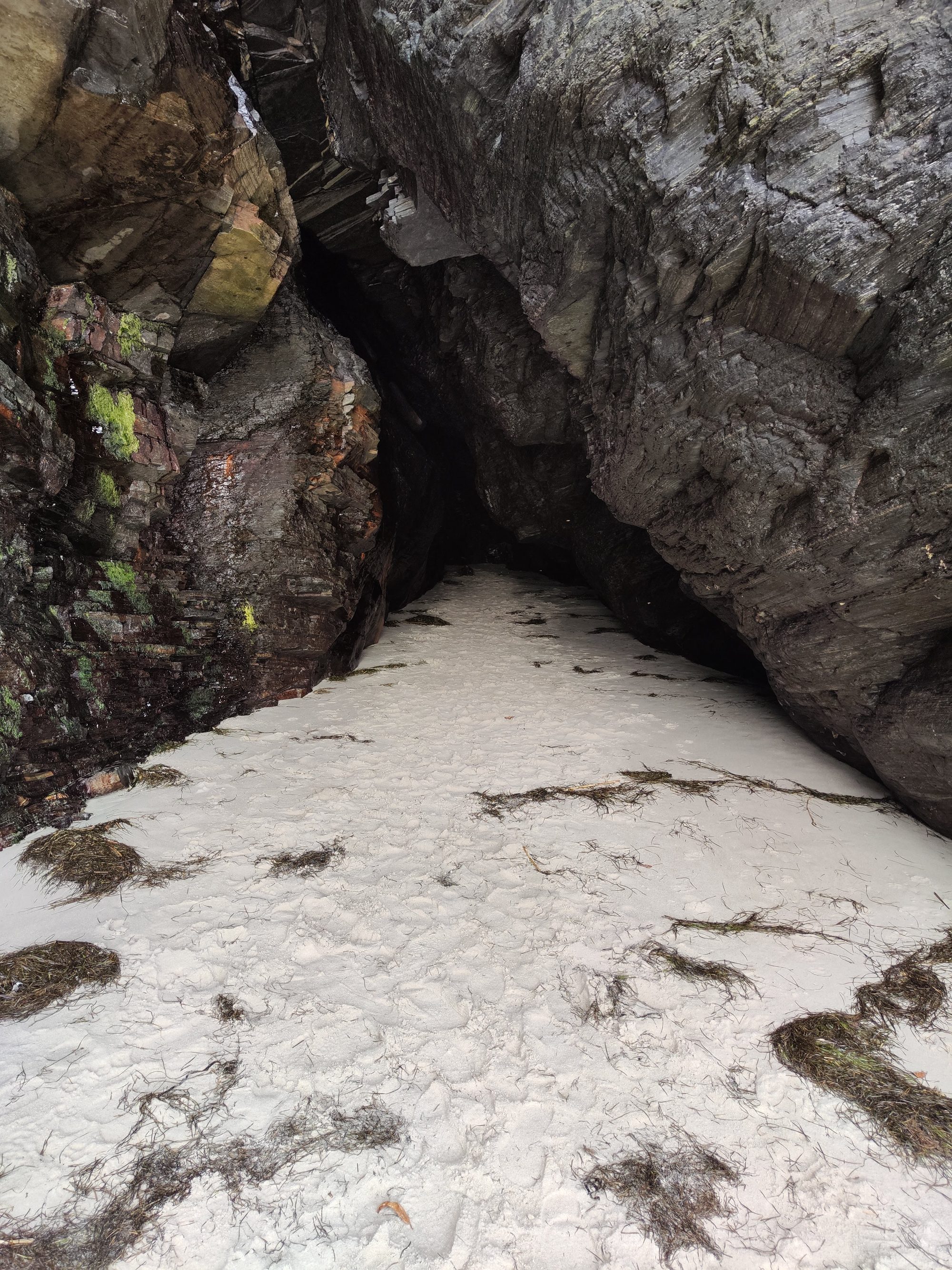 Entrada a una cueva marina entre oscuros acantilados de roca y arena blanca.