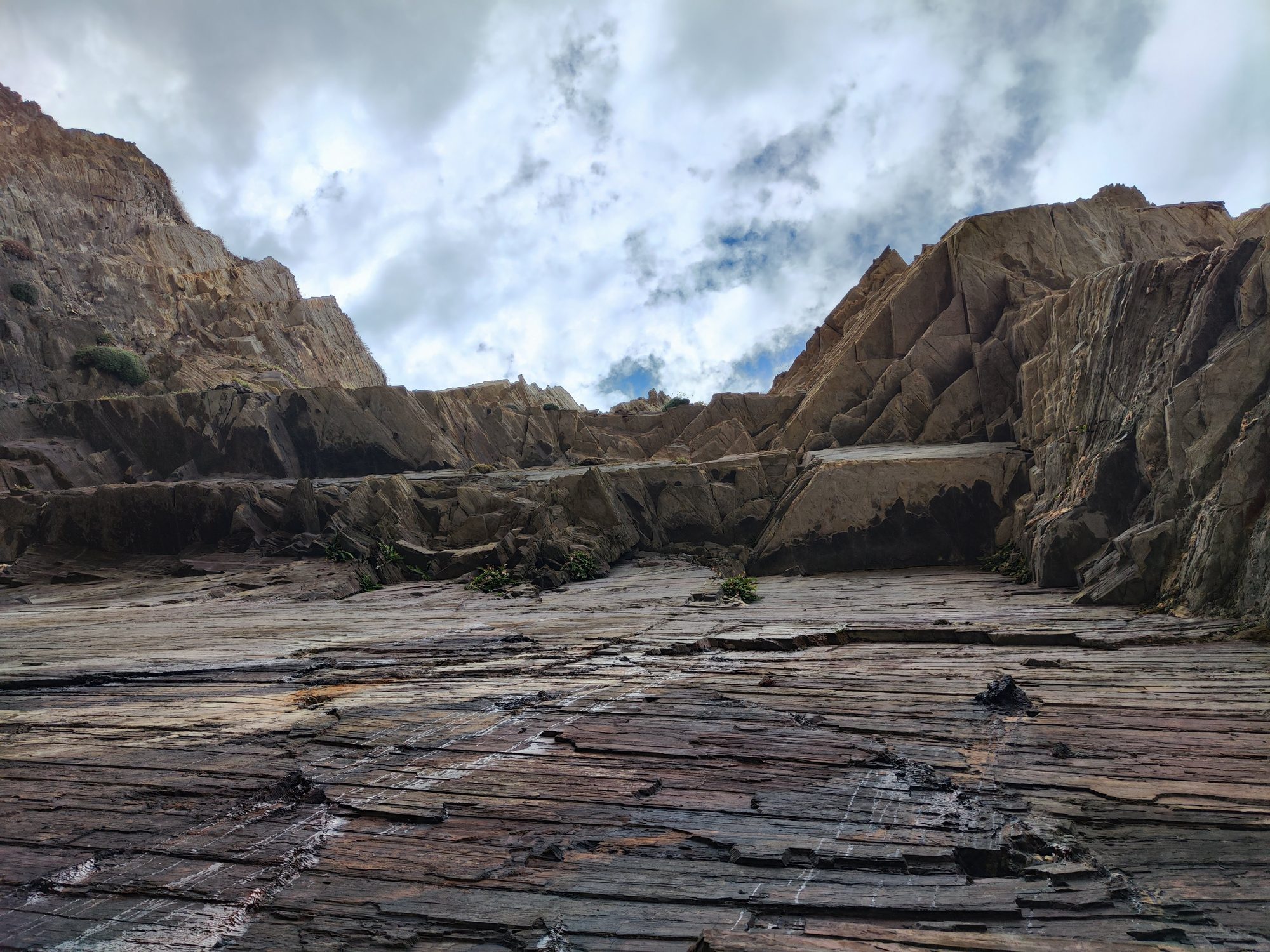 Formaciones rocosas estratificadas y acantilados escarpados bajo un cielo nublado en la costa.