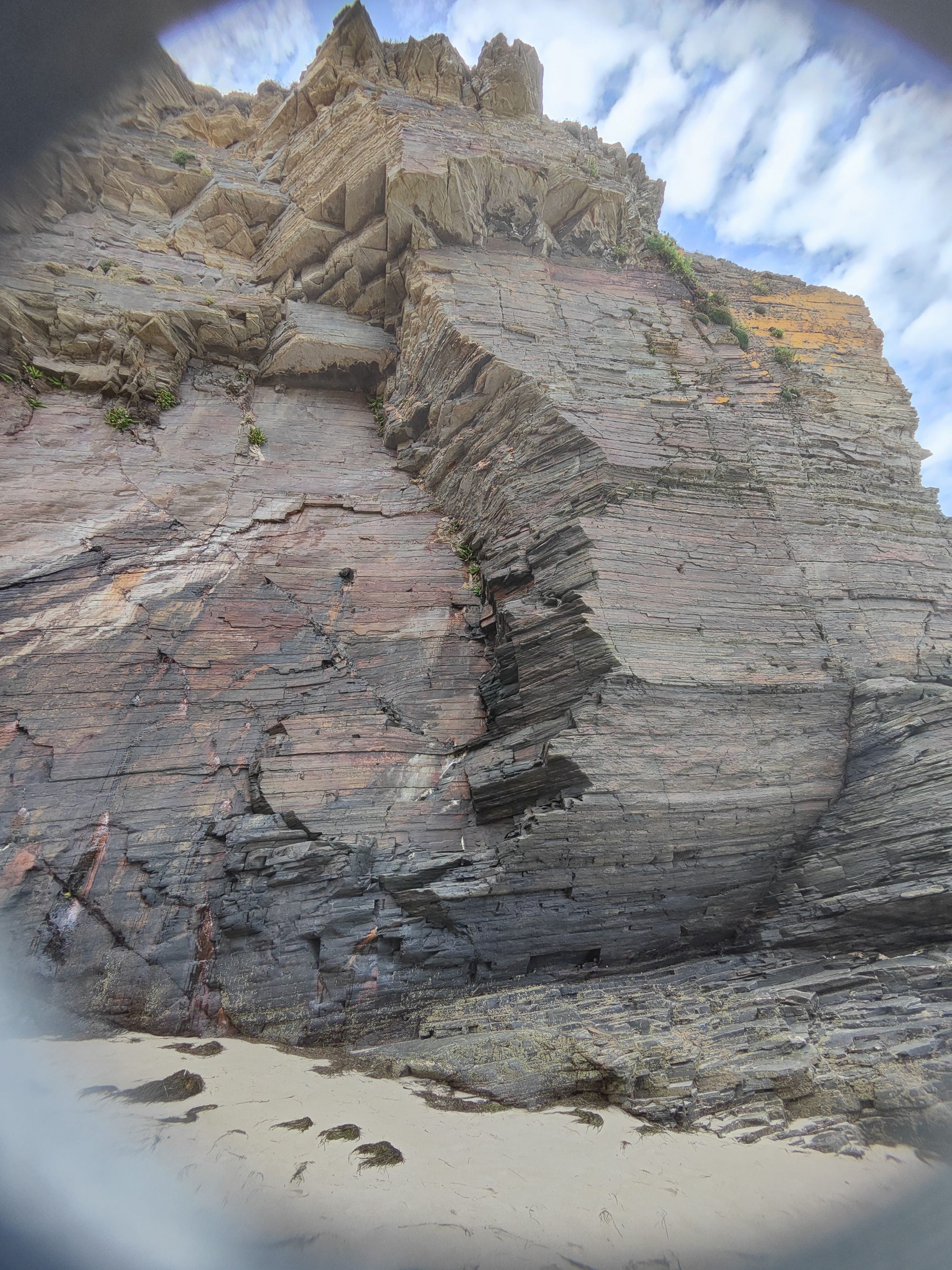 Imponente acantilado rocoso con marcados estratos geológicos en una playa de Ribadeo.
