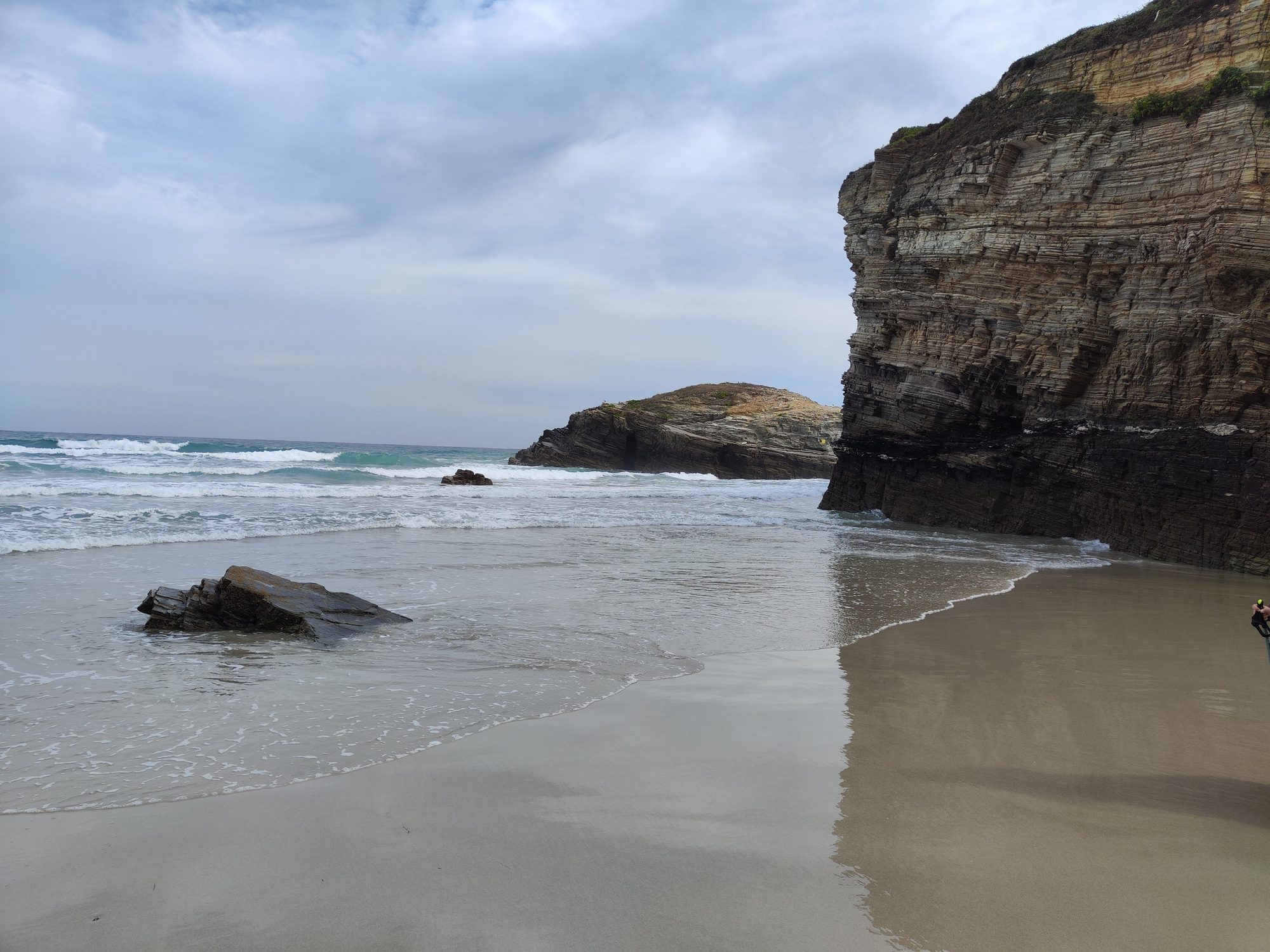 Acantilados de roca estratificada y olas rompiendo en la orilla de la playa.