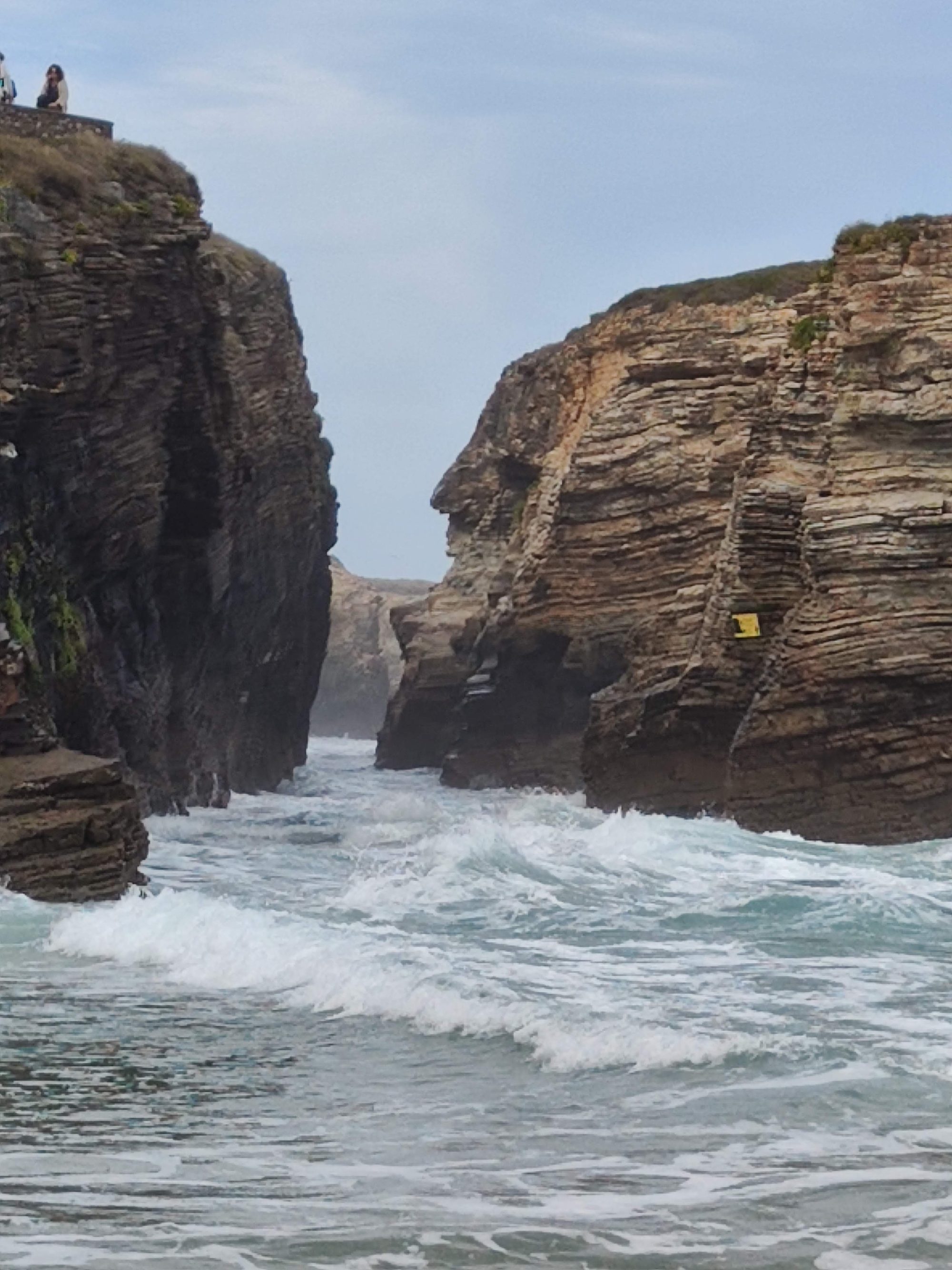 Olas del mar entrando con fuerza entre altos acantilados rocosos estratificados en la costa.