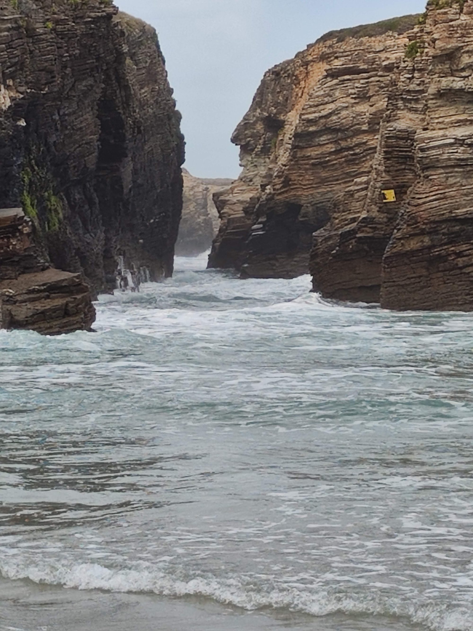 Olas del mar entrando con fuerza entre acantilados rocosos escarpados en la costa.