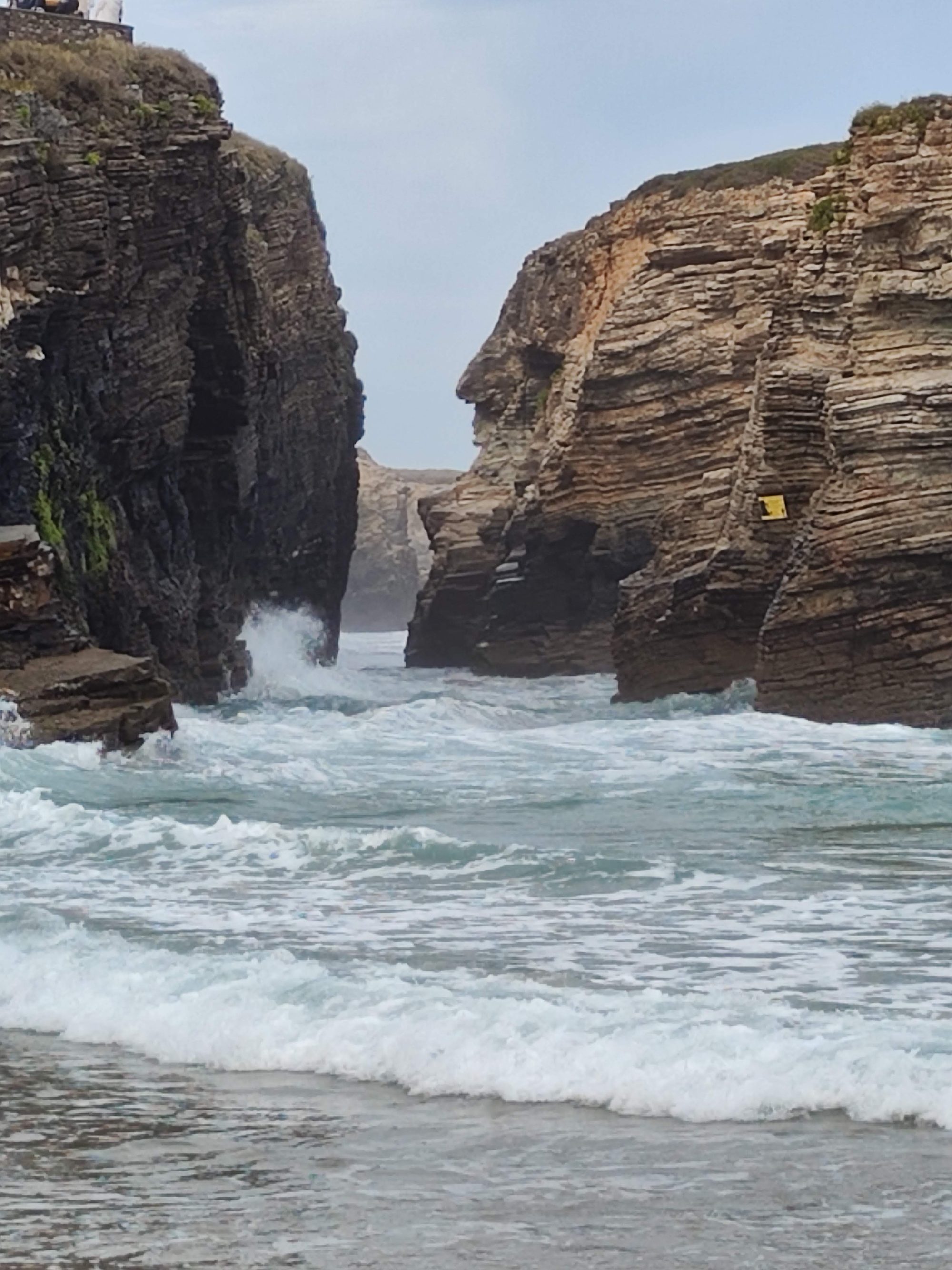 Olas rompiendo con fuerza entre altos acantilados de roca estratificada en la costa.