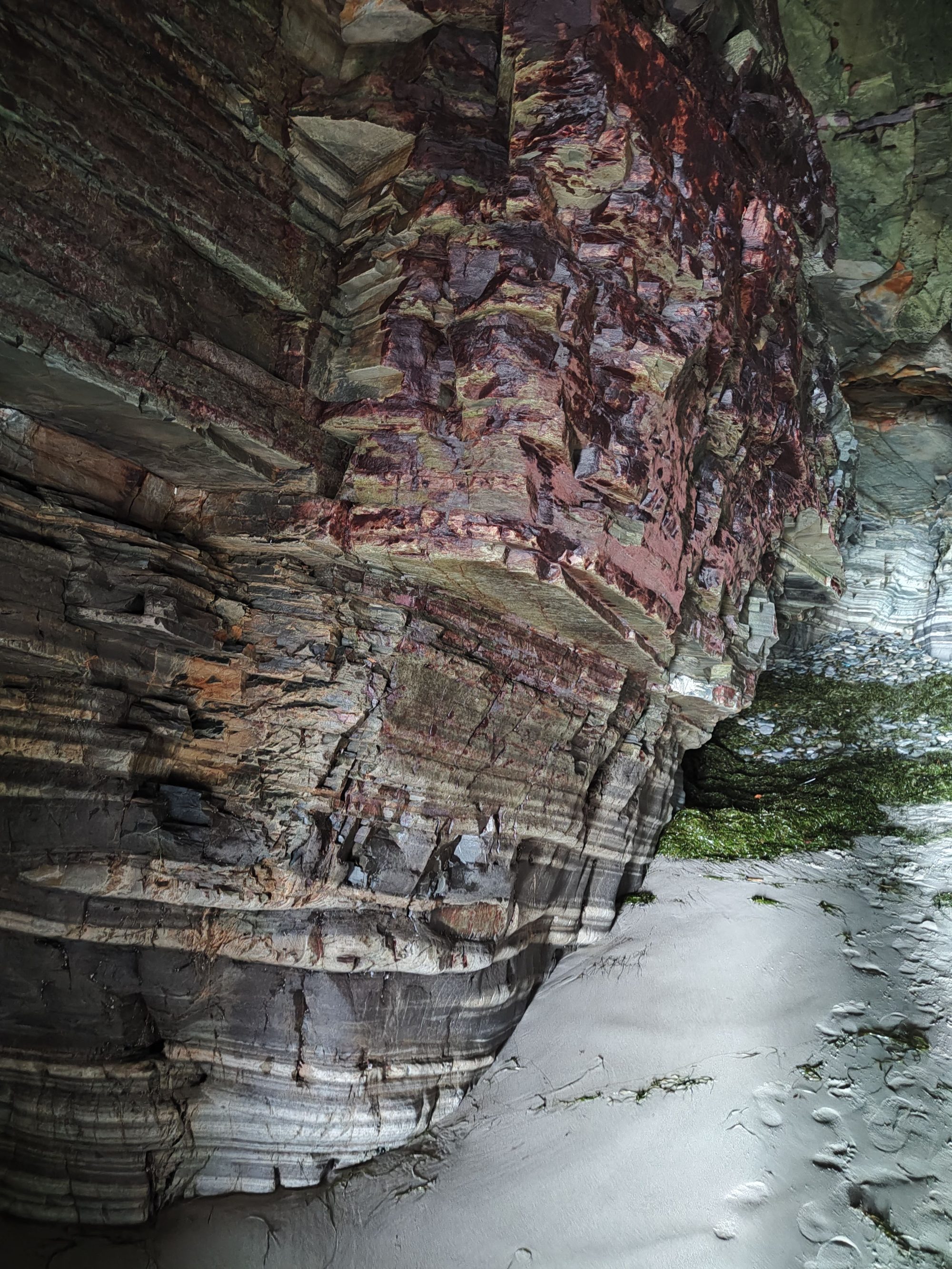 Paredes rocosas estratificadas y arena húmeda en el interior de una cueva marina.