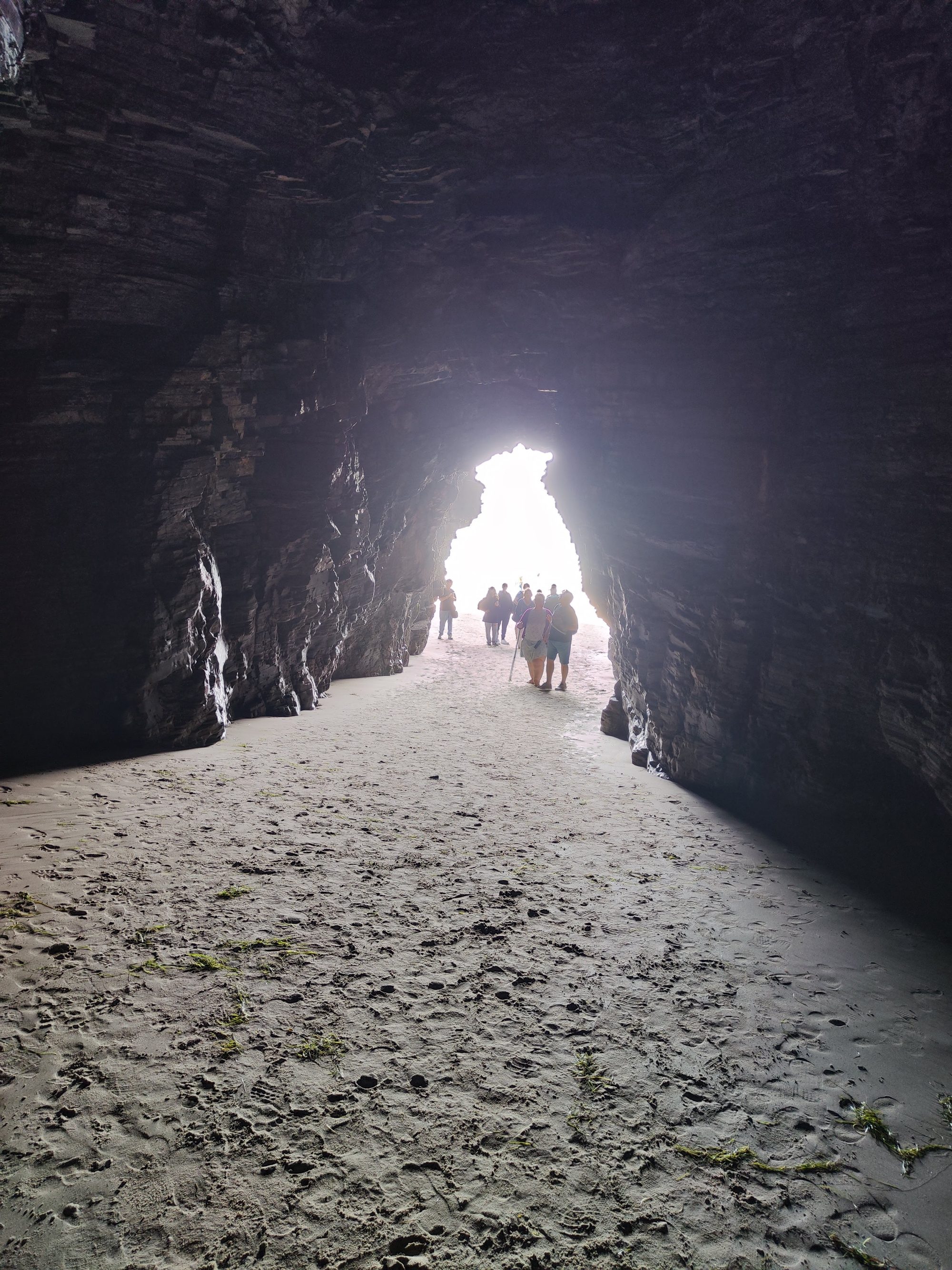 Vista desde el interior de una cueva marina de roca hacia la playa iluminada.