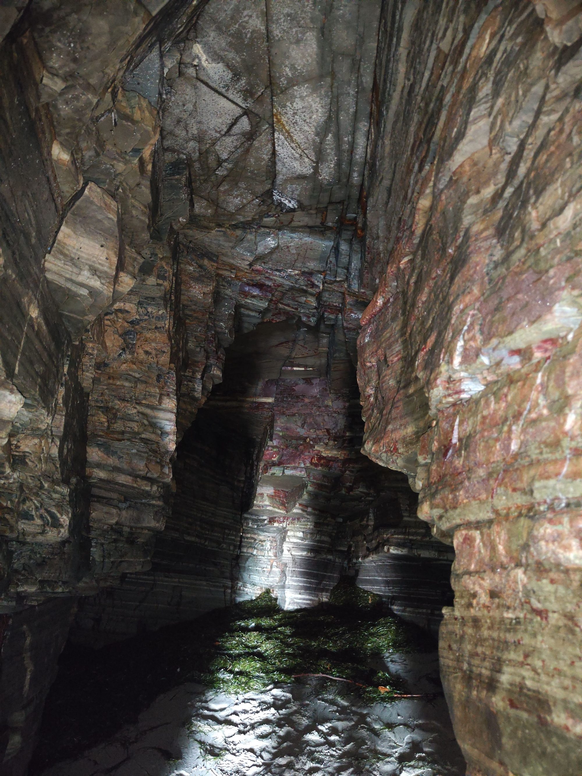 Interior de una cueva marina con paredes rocosas estratificadas y suelo de arena.