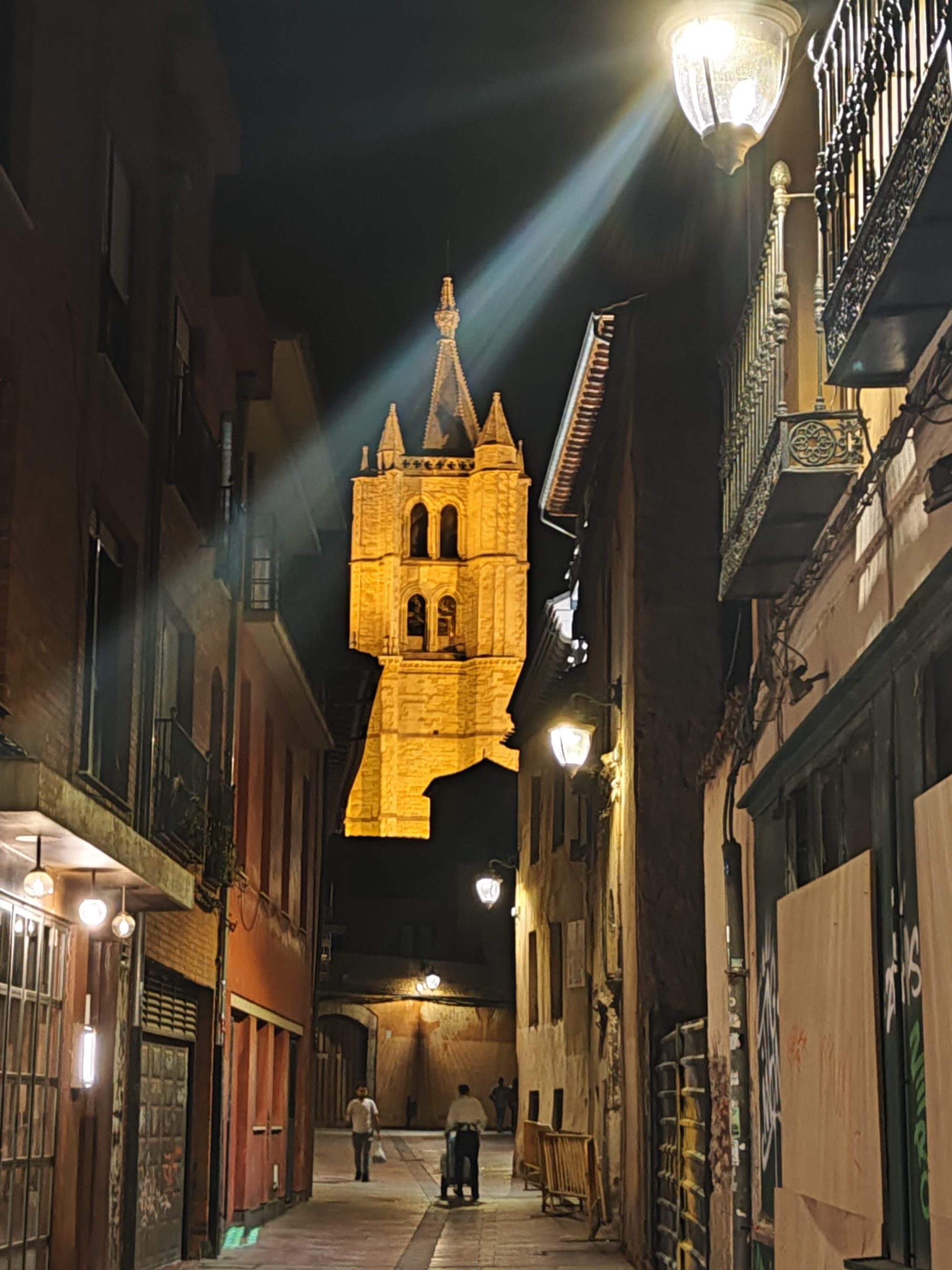 Torre iluminada de la Catedral de León vista desde una estrecha calle nocturna.