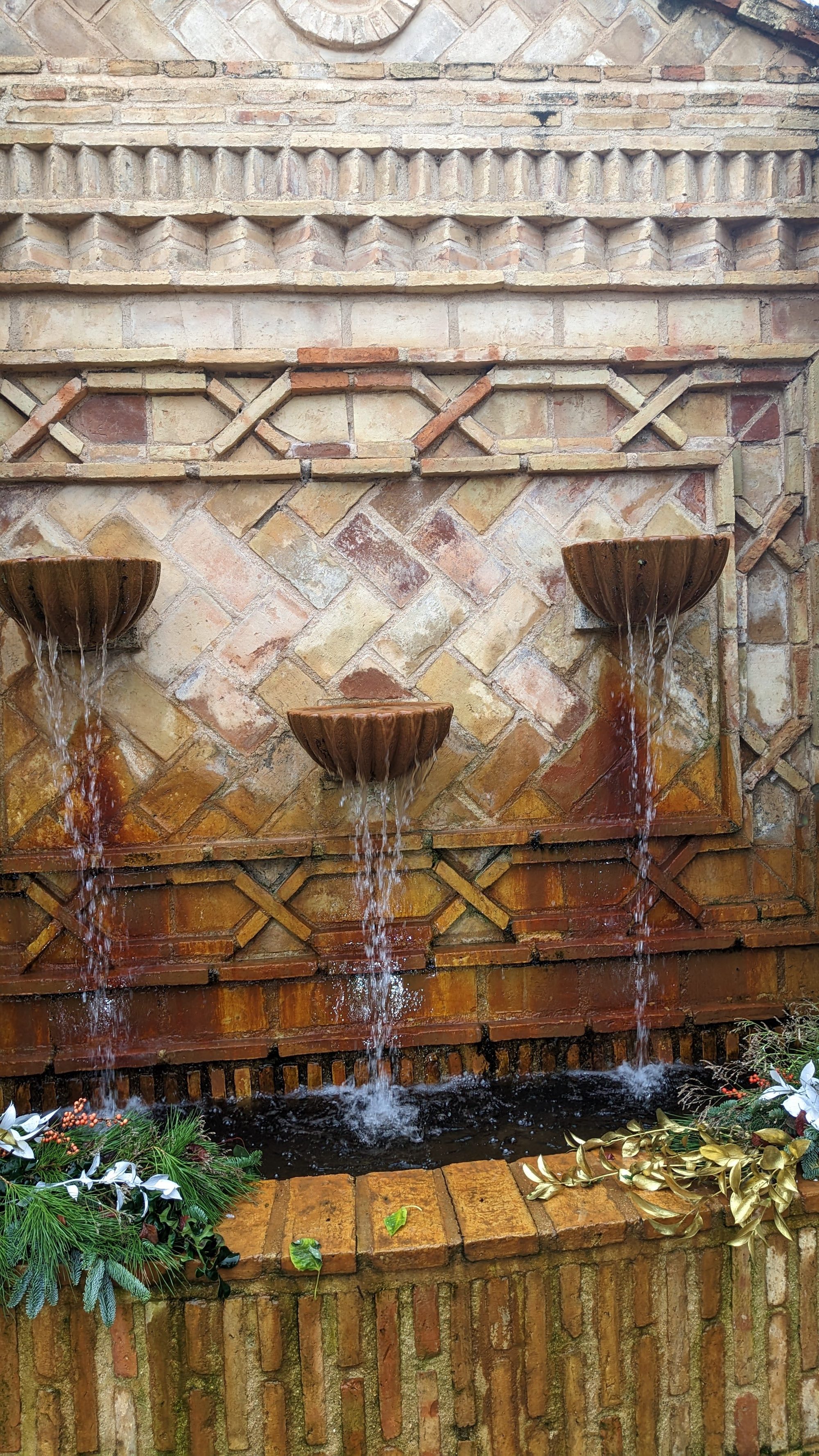 Fuente mural de ladrillo con tres vertedores de agua y decoración vegetal en la base.