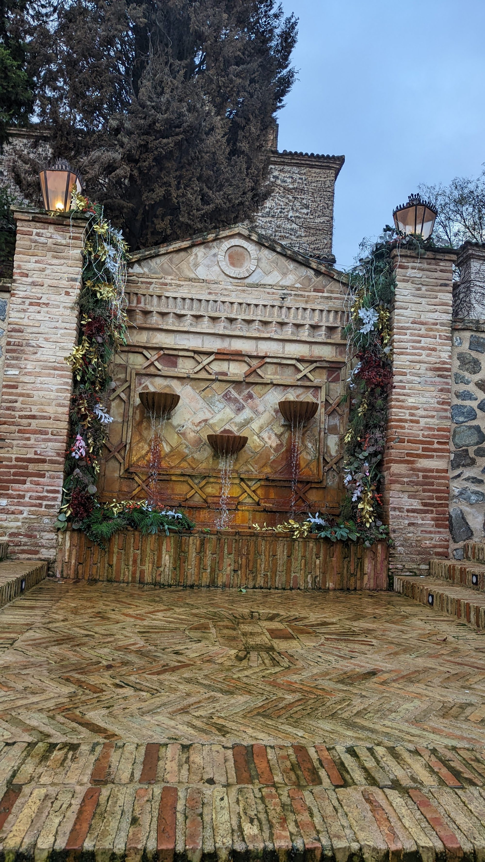 Fuente de ladrillo visto con tres caños y adornos navideños en un patio toledano.