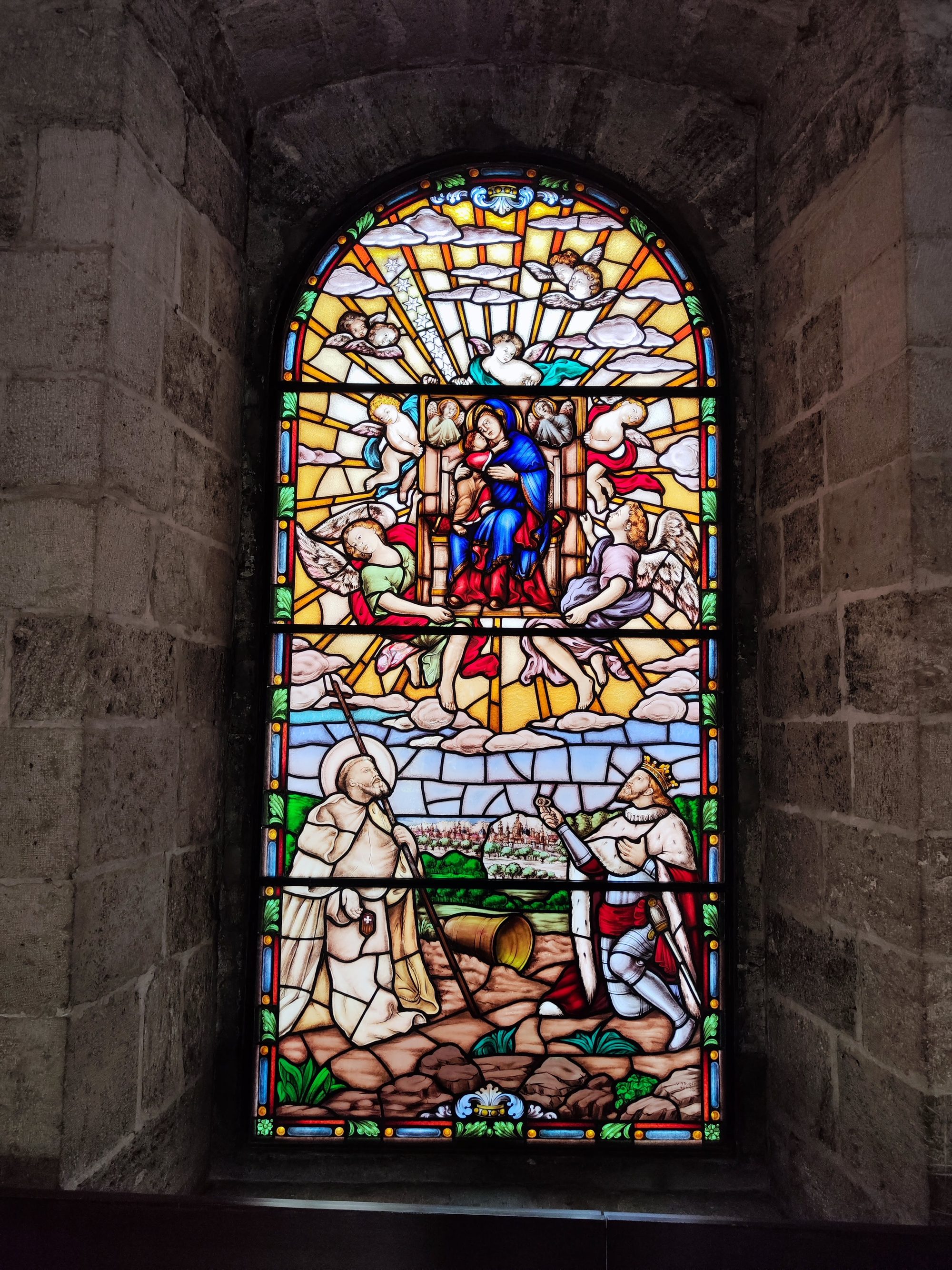 Vidriera de colores con escenas religiosas enmarcada en un arco de piedra antigua.