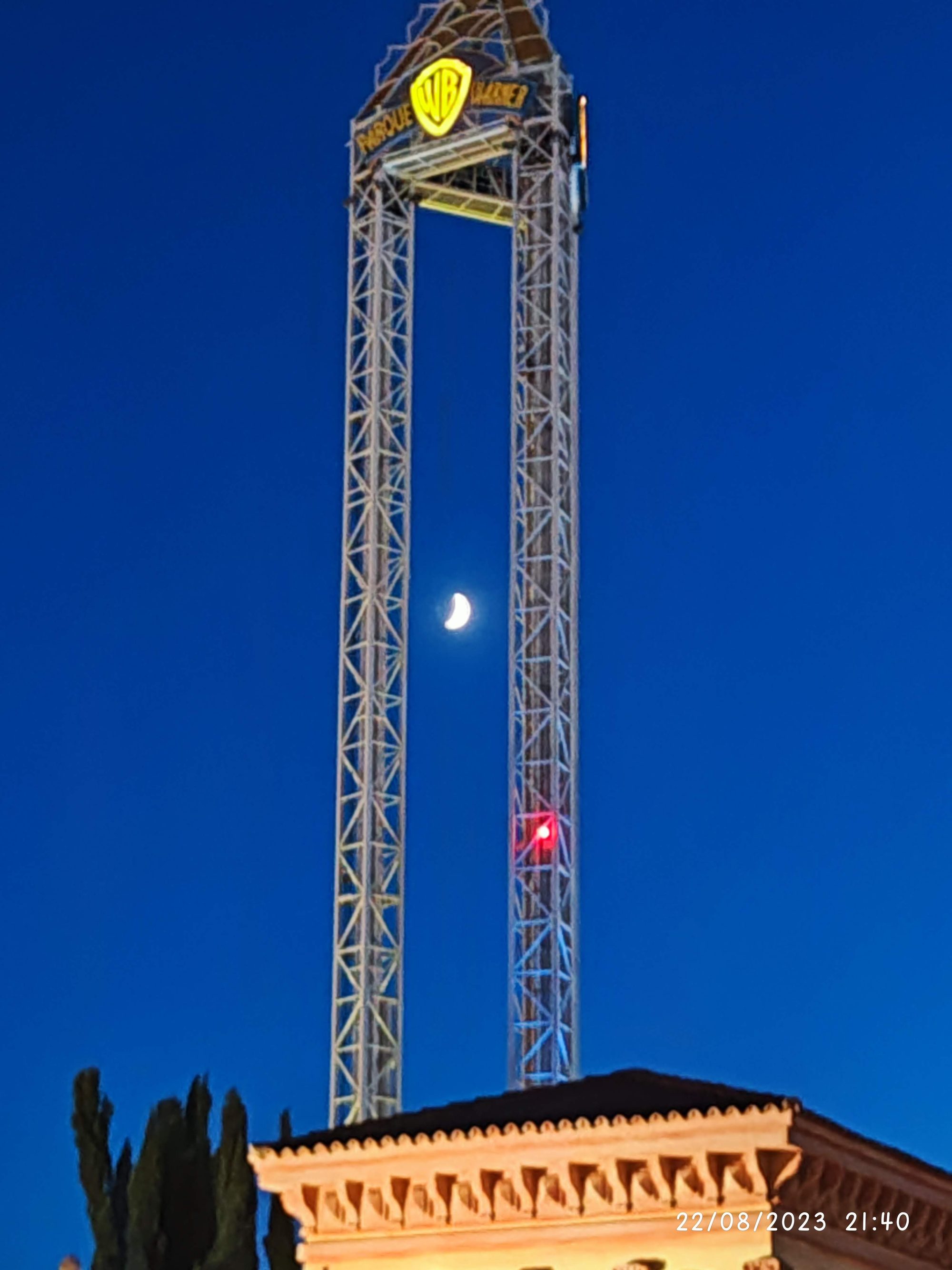 Torre metálica de Parque Warner al anochecer con la luna creciente entre sus estructuras.