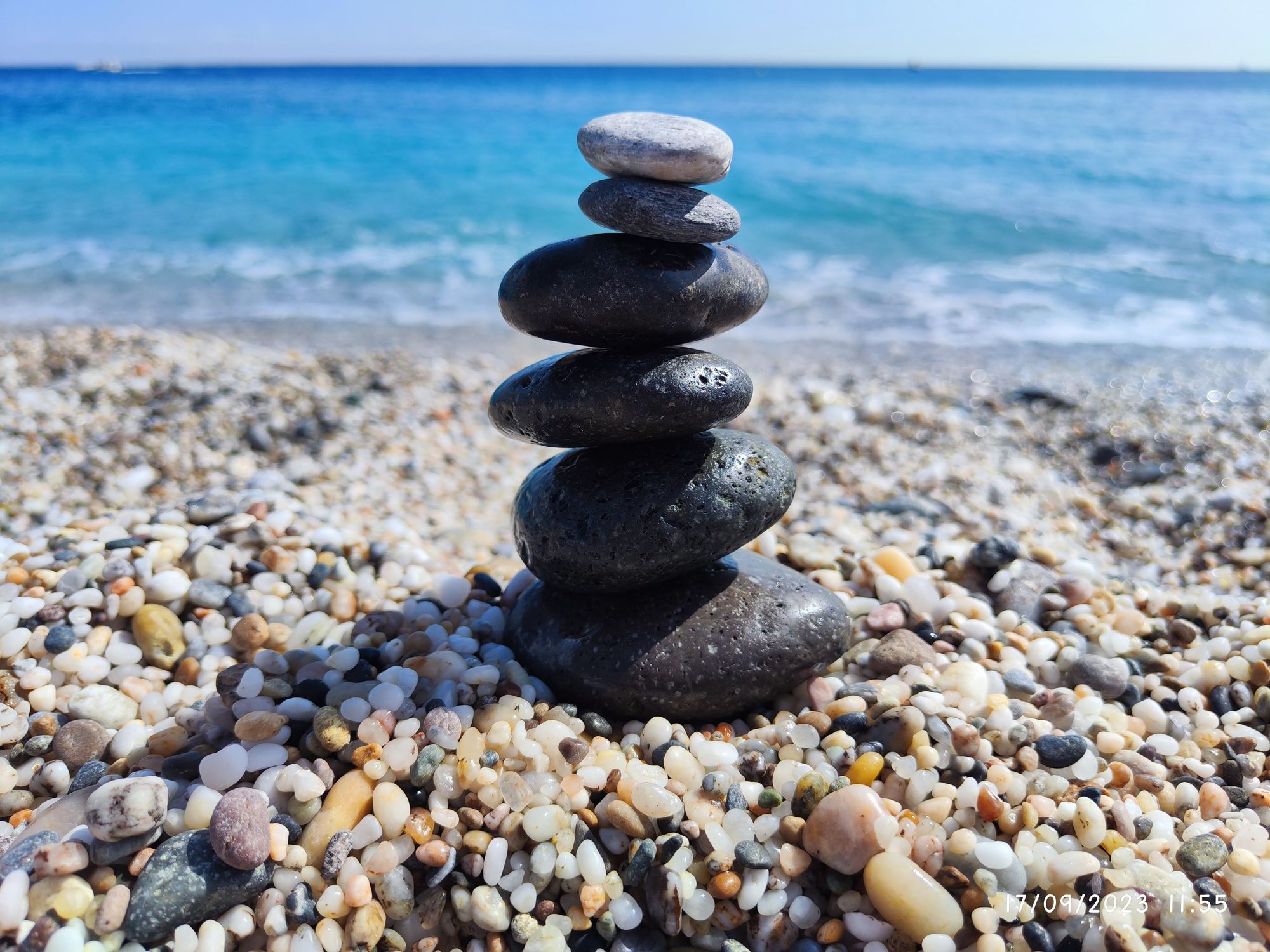Piedras apiladas en equilibrio sobre una playa de guijarros frente al mar azul.