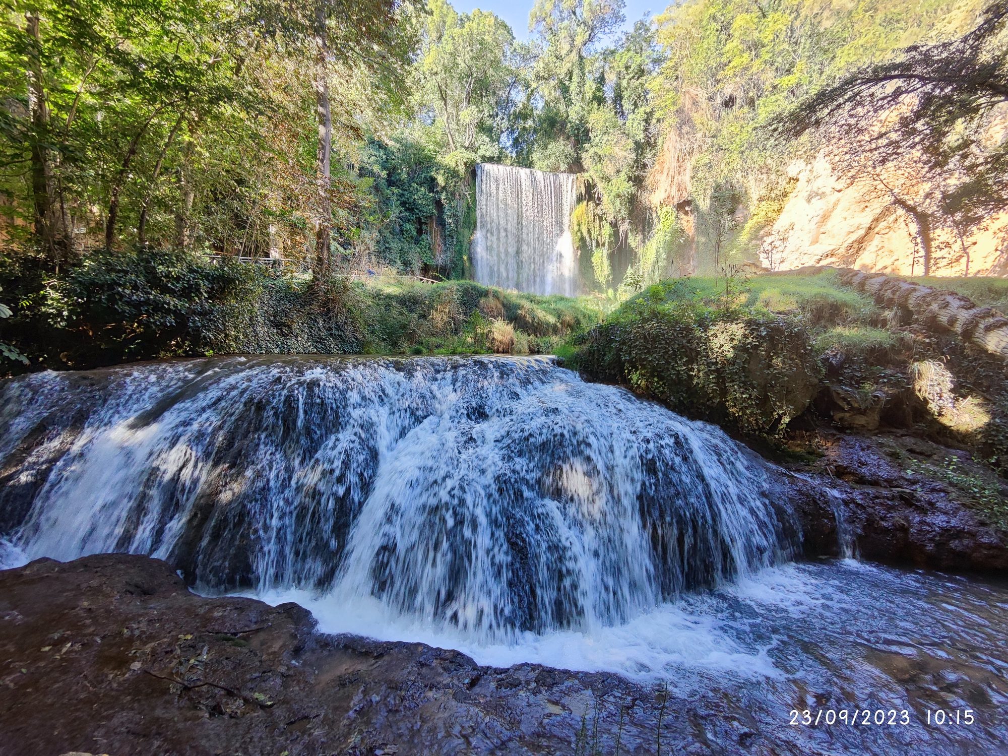 Cascadas de agua fluyendo entre exuberante vegetación verde y rocas en un entorno natural.