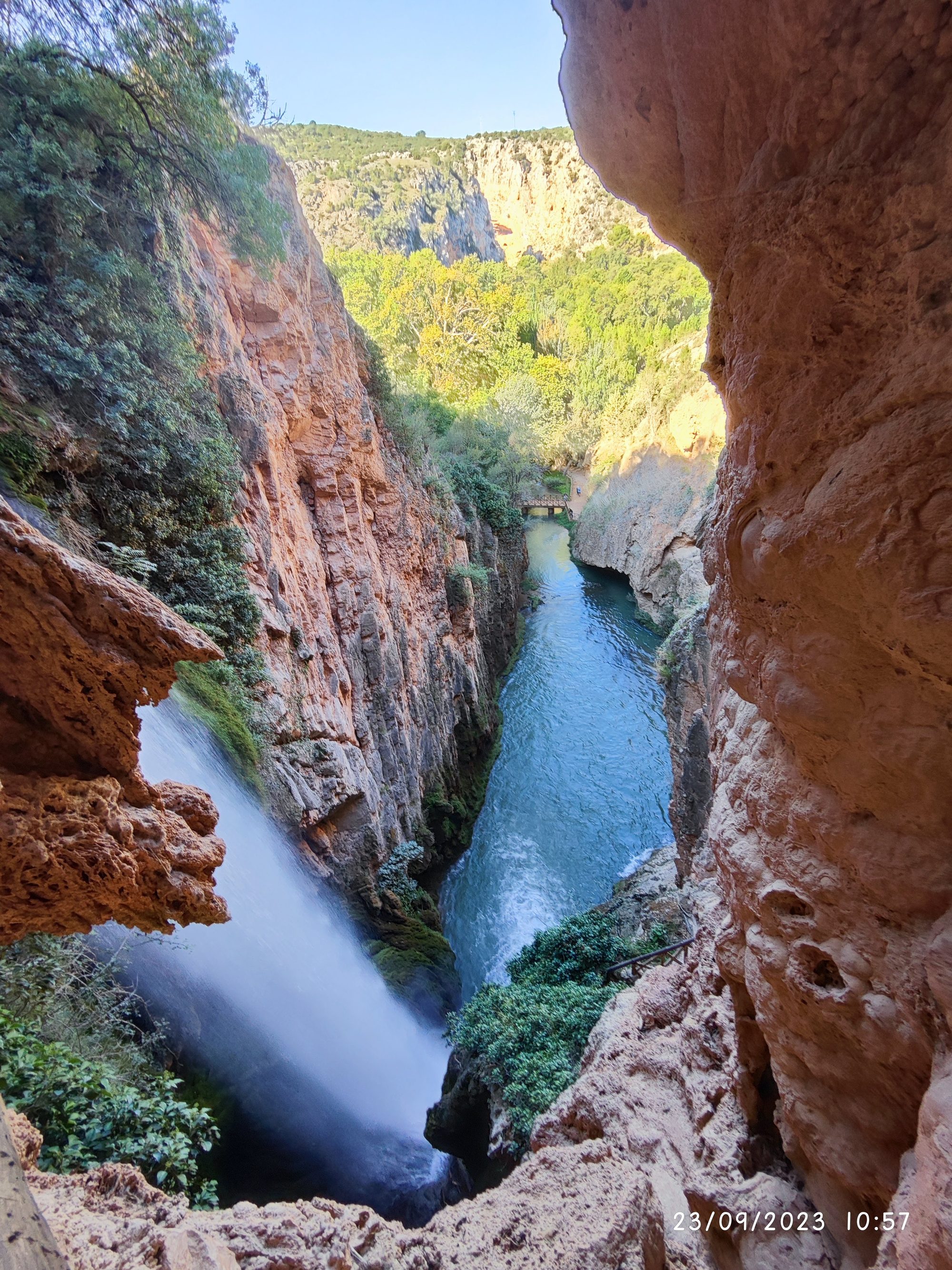 Vista desde una cueva hacia una impresionante cascada entre cañones rocosos.