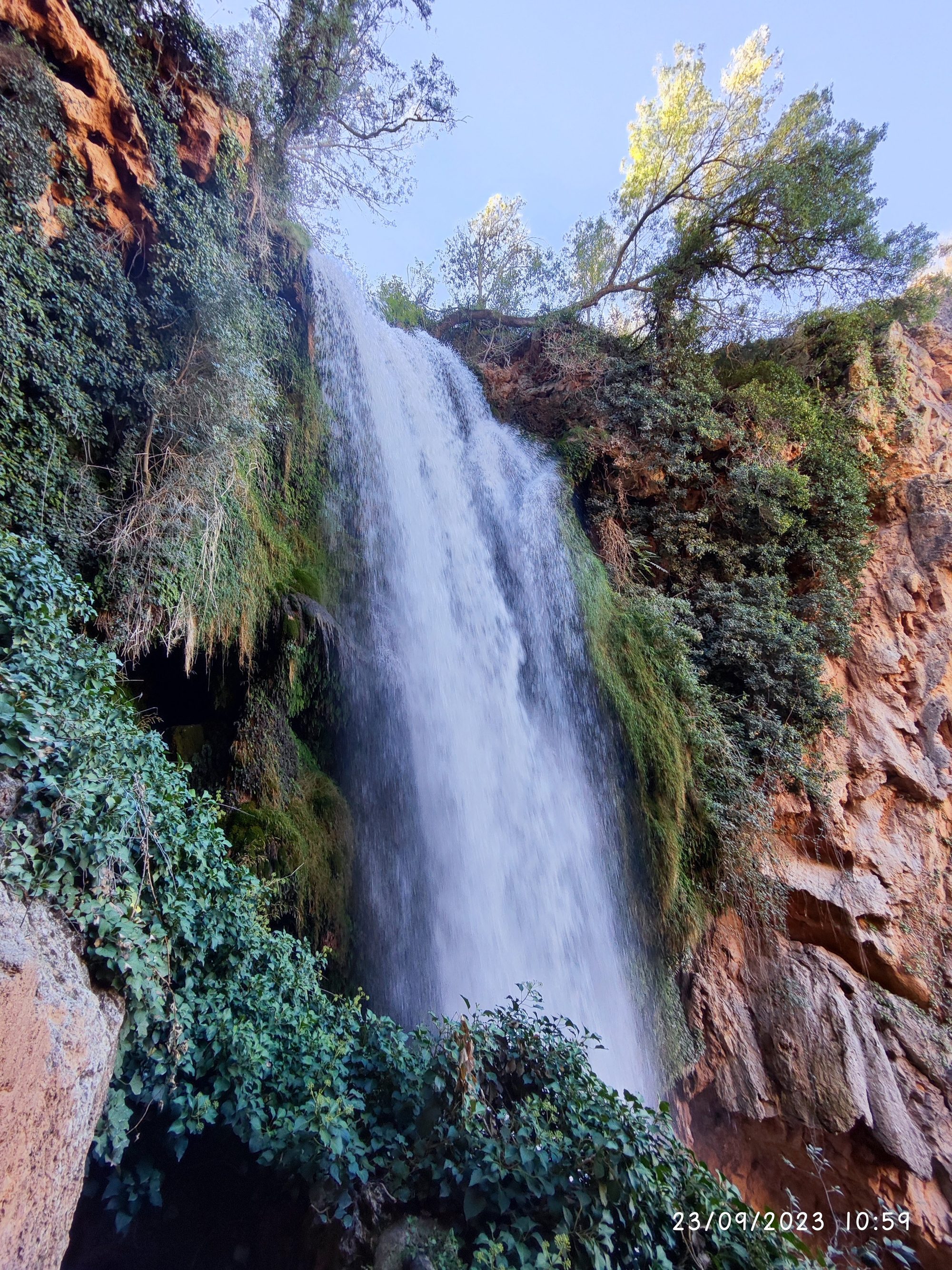 Gran cascada de agua entre rocas rojizas y frondosa vegetación verde.
