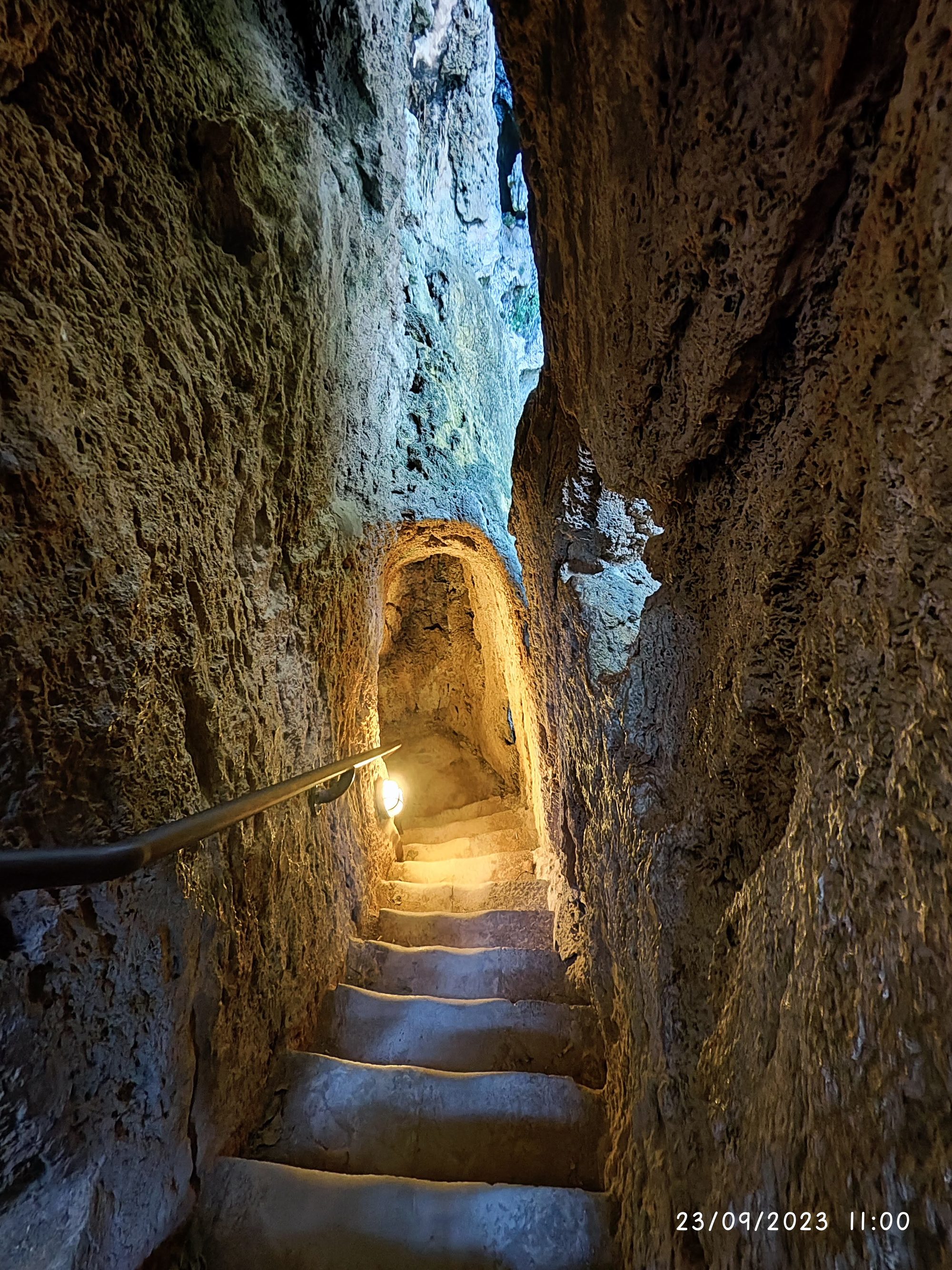 Escalera de piedra iluminada en un pasadizo estrecho dentro de una cueva de roca.