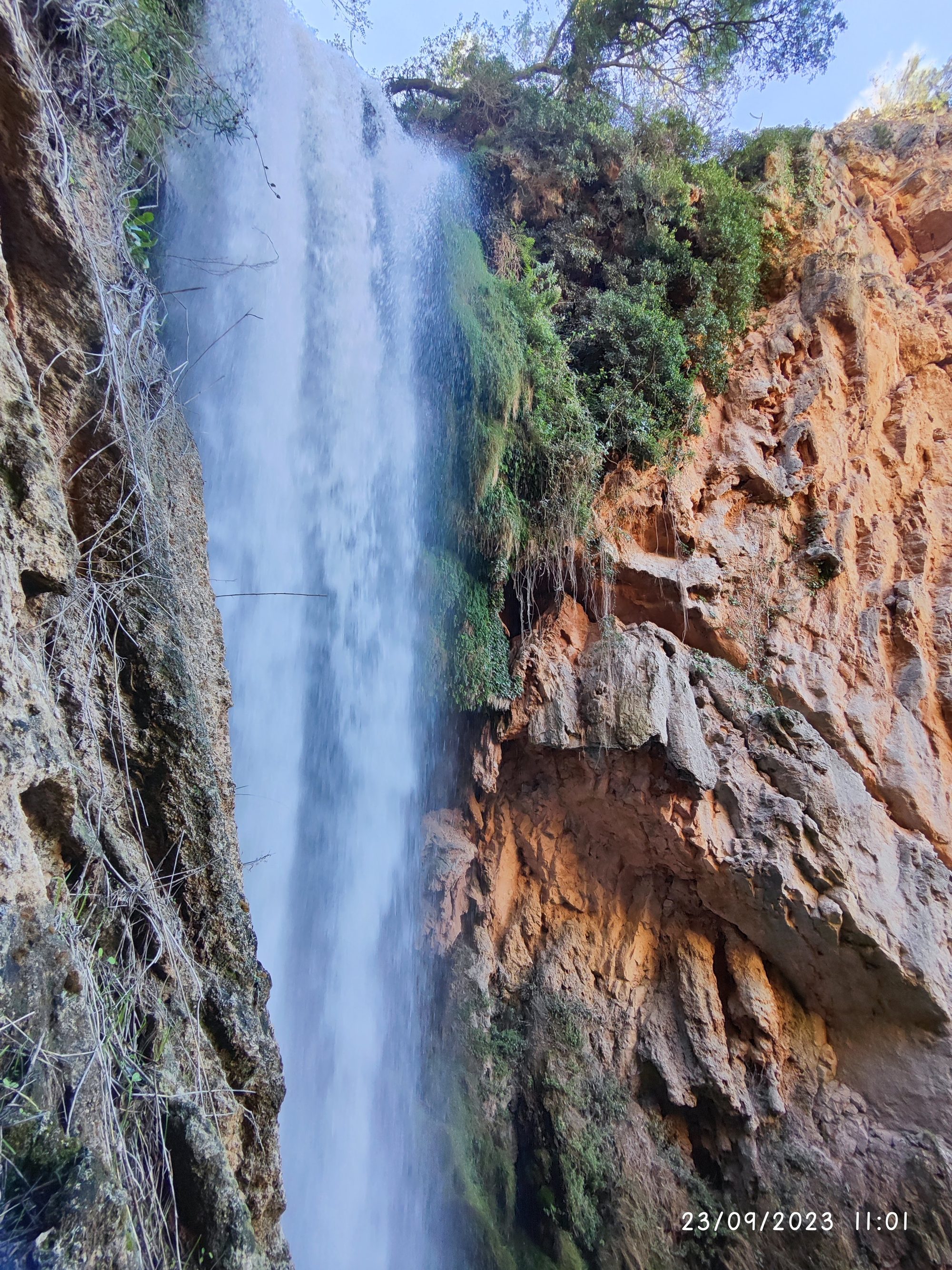 Gran cascada de agua cayendo entre paredes de roca rojiza con vegetación.
