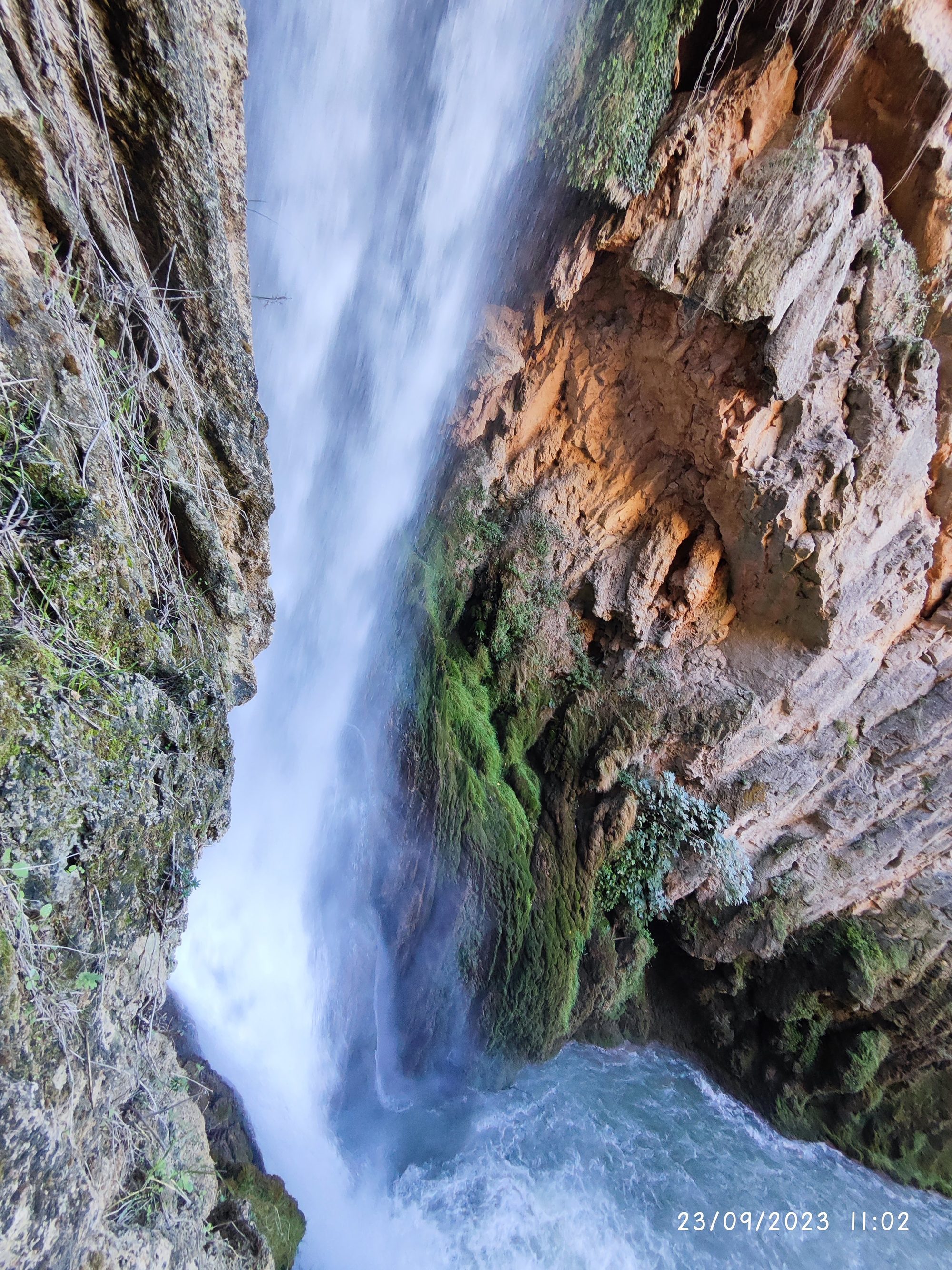 Gran cascada de agua entre paredes rocosas y acantilados cubiertos de musgo verde