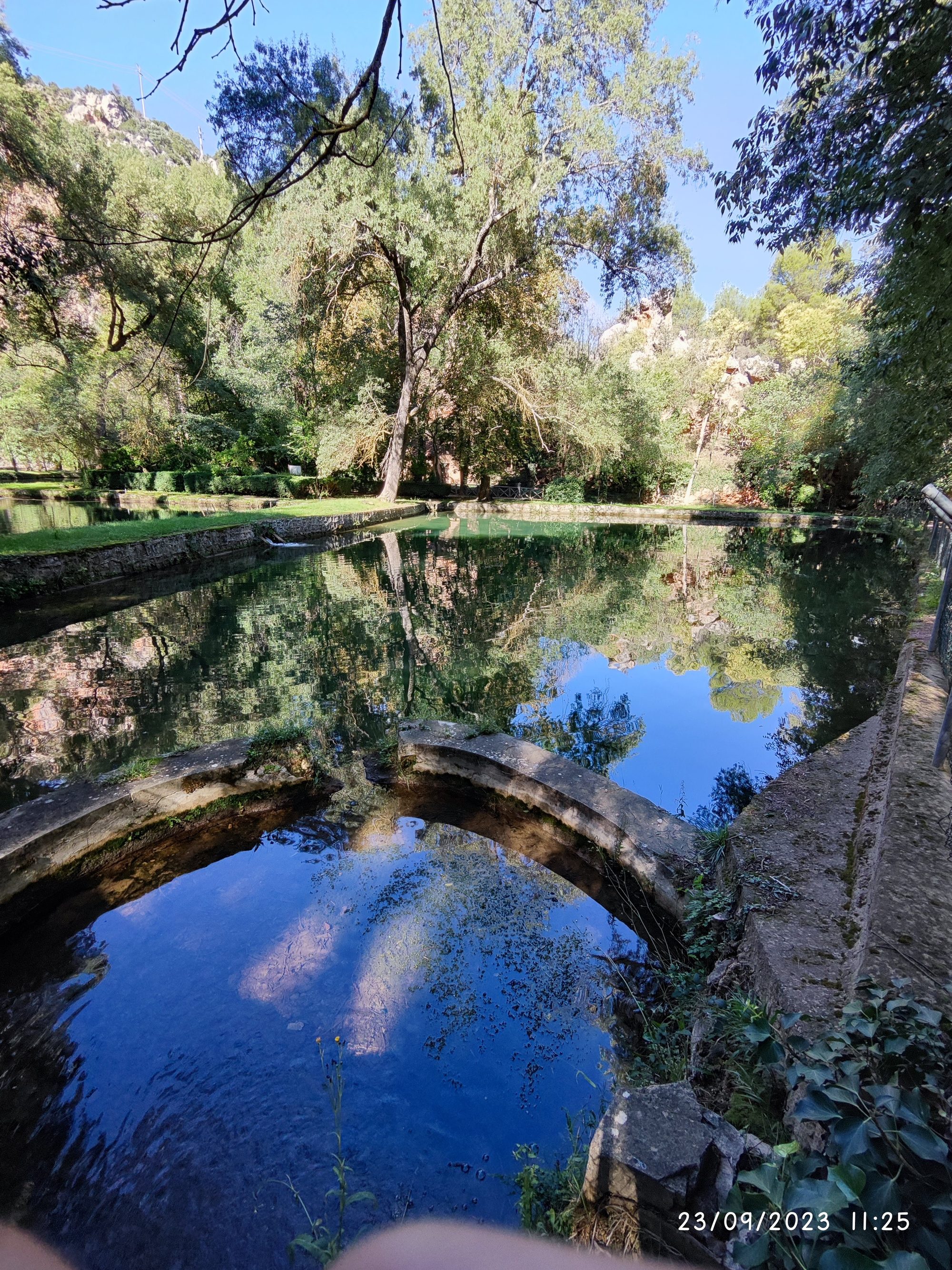 Estanque de agua cristalina con reflejos de árboles y cielo azul en Nuévalos.