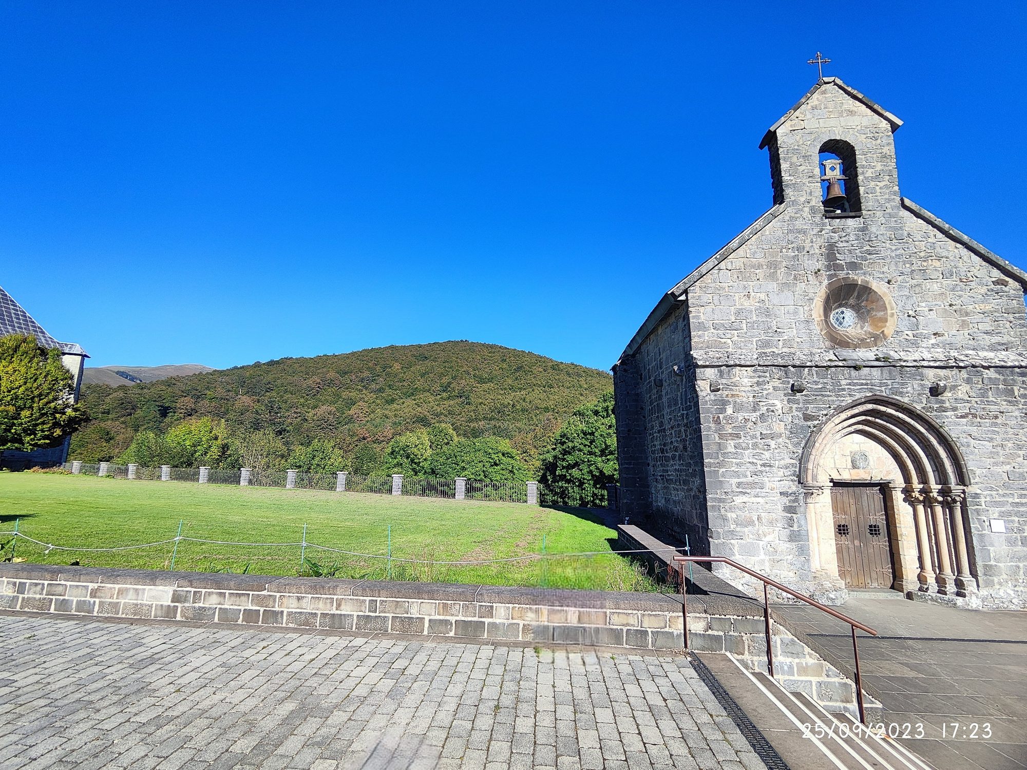 Capilla de piedra medieval en Roncesvalles con fondo de colinas verdes y cielo azul.