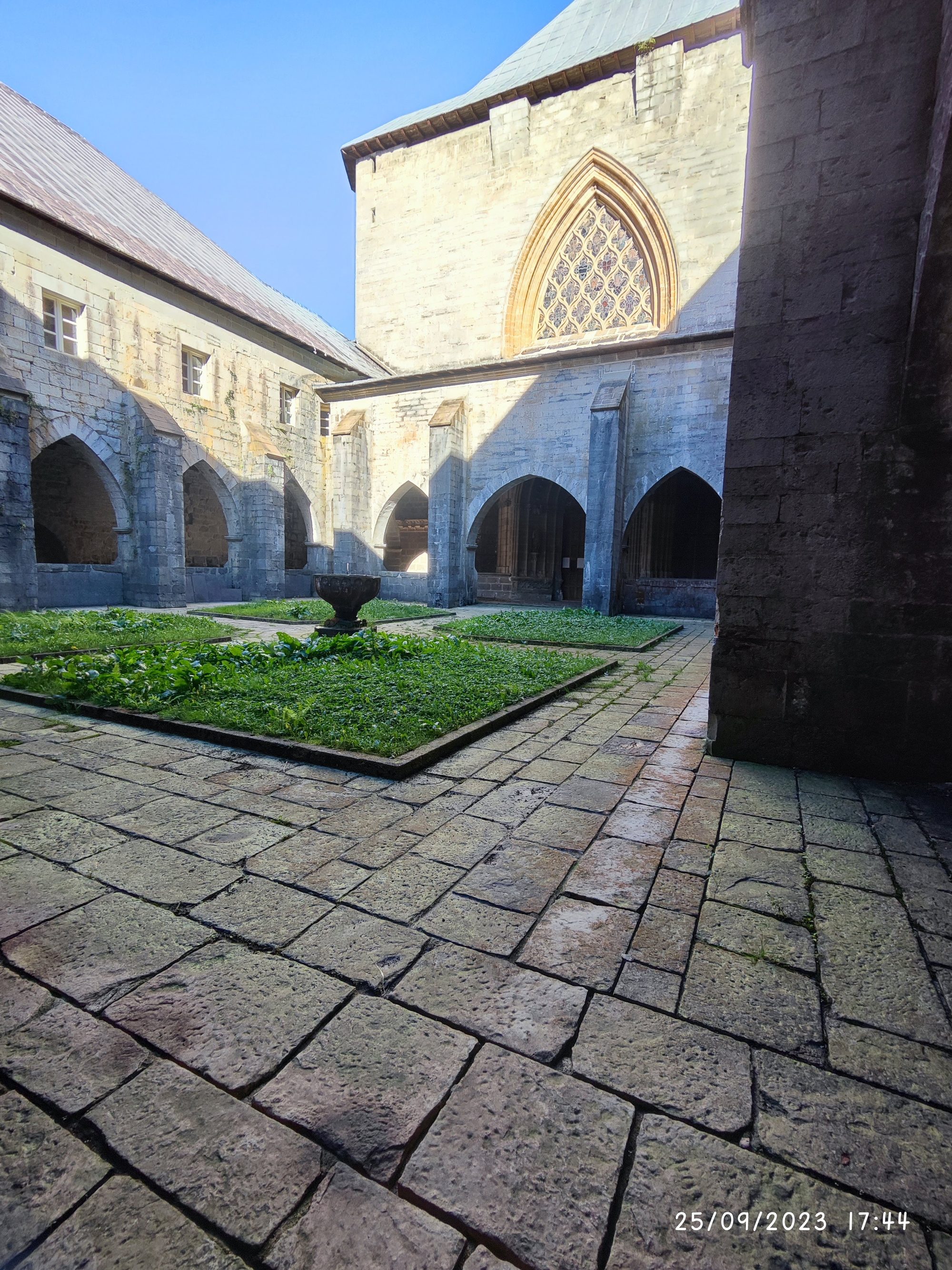Claustro gótico de piedra con arcos y jardín interior bajo un cielo despejado.