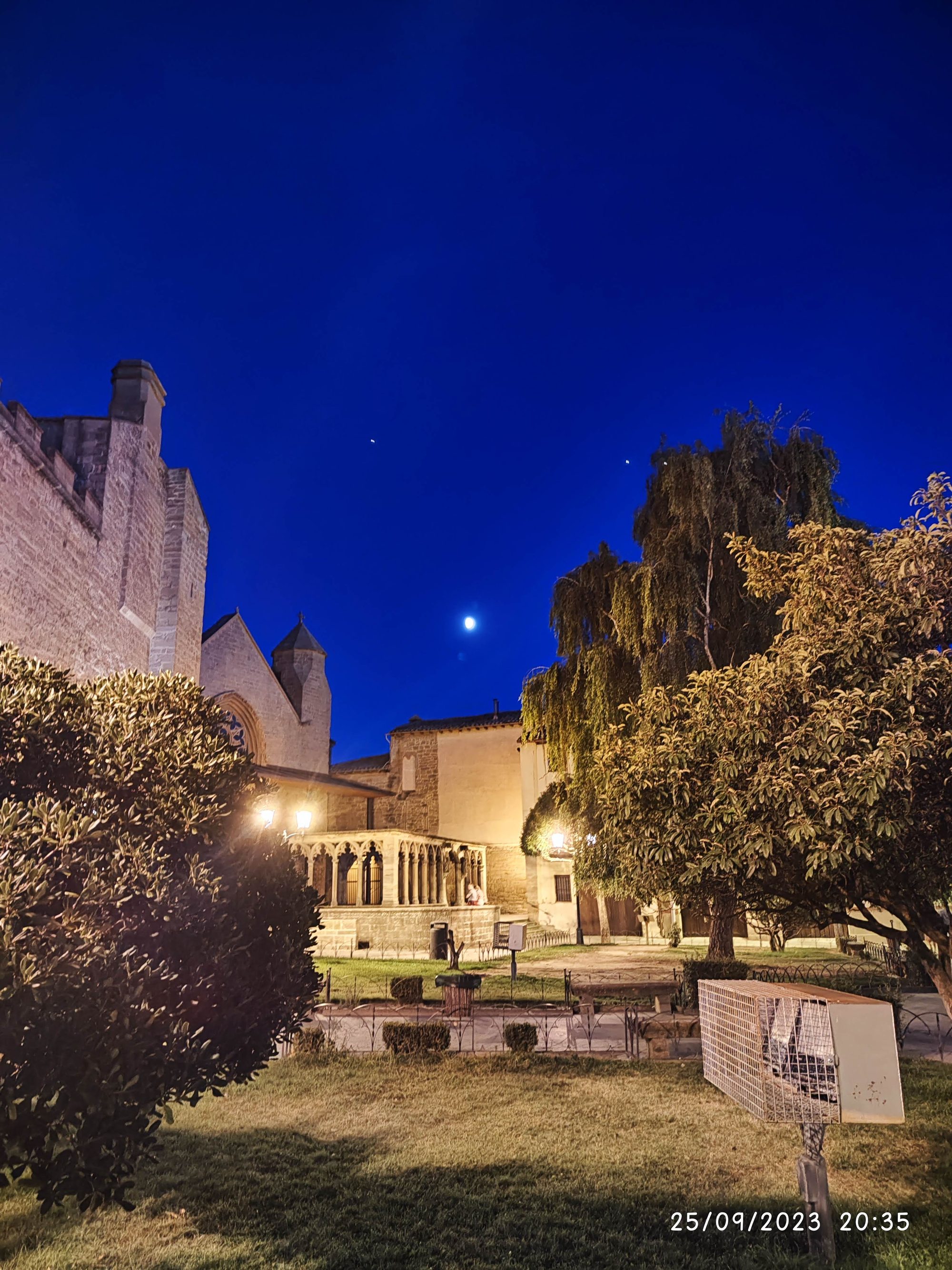 Claustro e iglesia de piedra iluminados de noche bajo un cielo azul profundo en Olite.