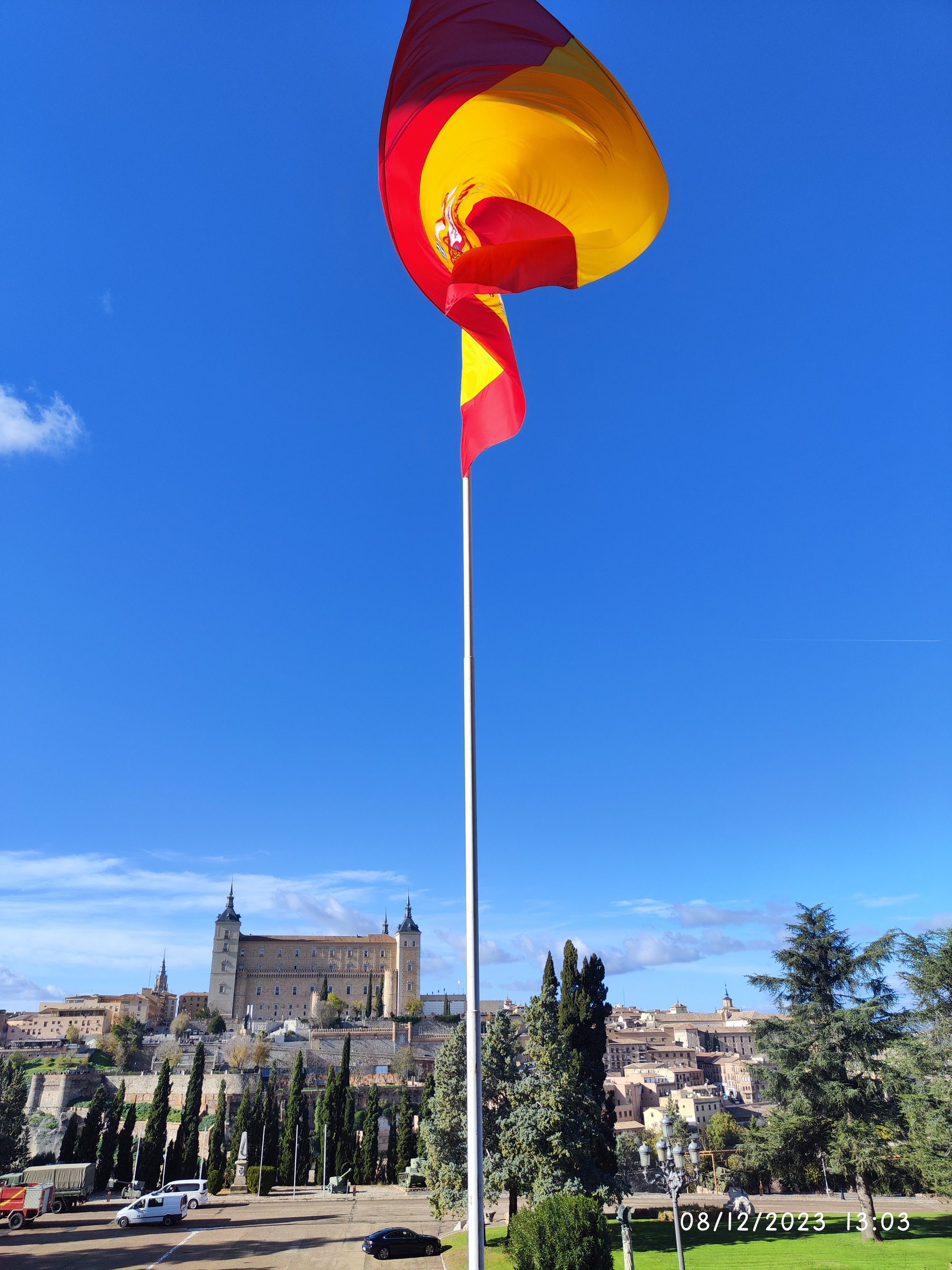 Gran bandera de España ondeando en un asta con Toledo y el Alcázar al fondo.