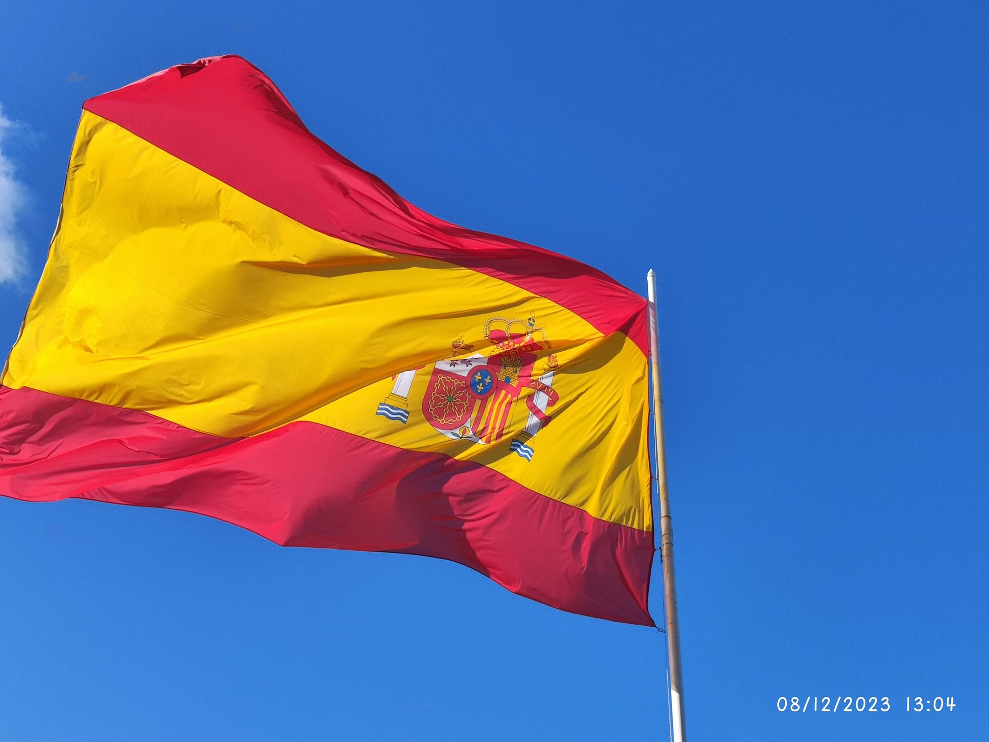 Bandera de España ondeando al viento sobre un fondo de cielo azul despejado.