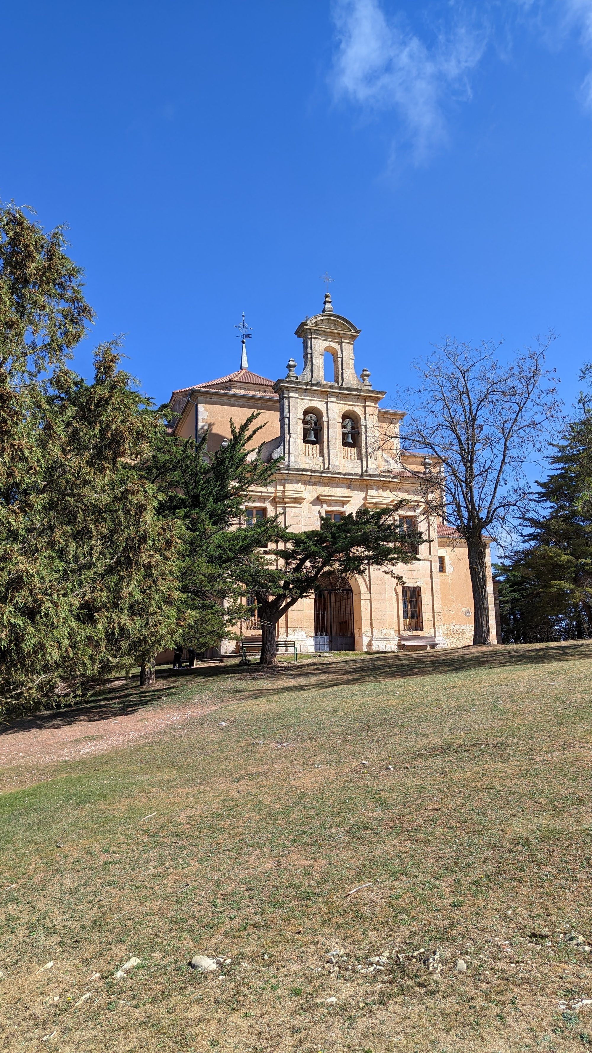Ermita de piedra con espadaña rodeada de árboles en Moral de Hornuez bajo cielo azul.