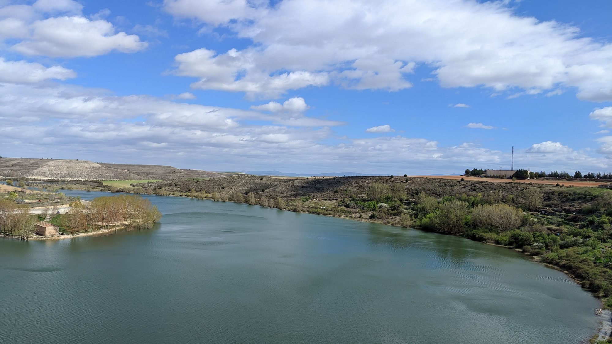 Embalse rodeado de colinas y vegetación bajo un cielo azul con nubes blancas.