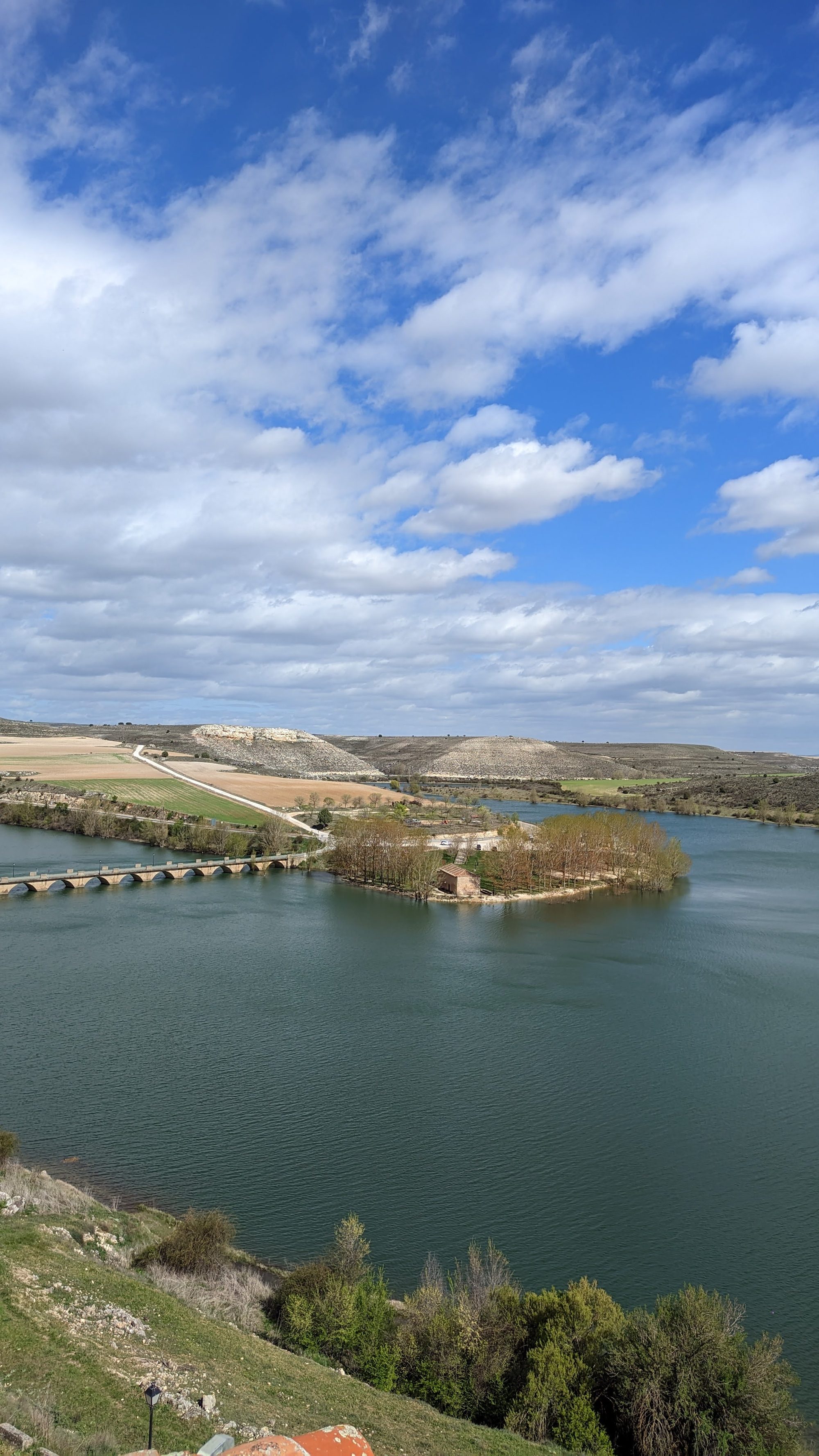 Vista panorámica del embalse de Maderuelo con su puente románico y colinas bajo cielo nublado.