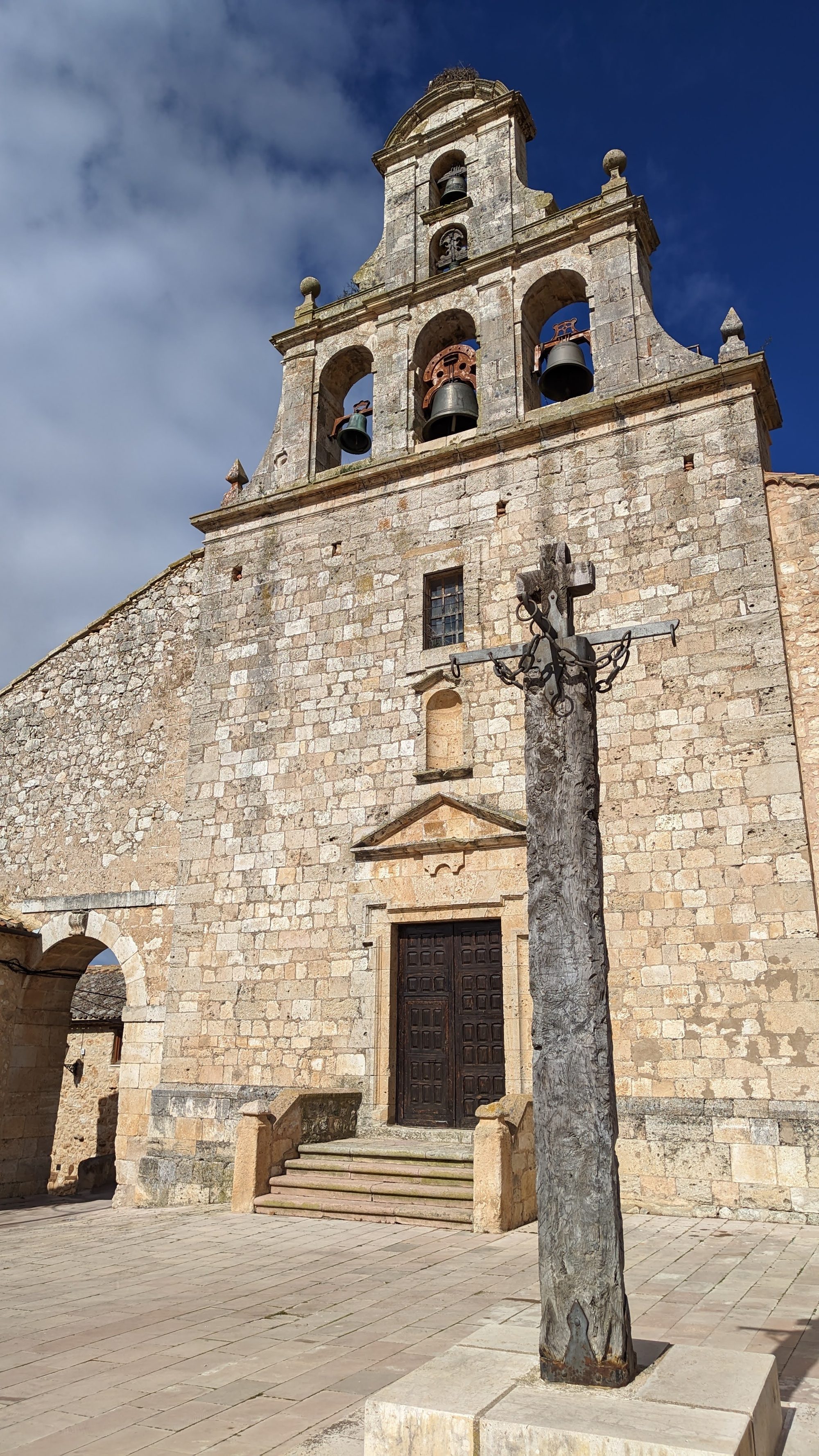 Espadaña de piedra de una iglesia medieval con una cruz de madera delante.