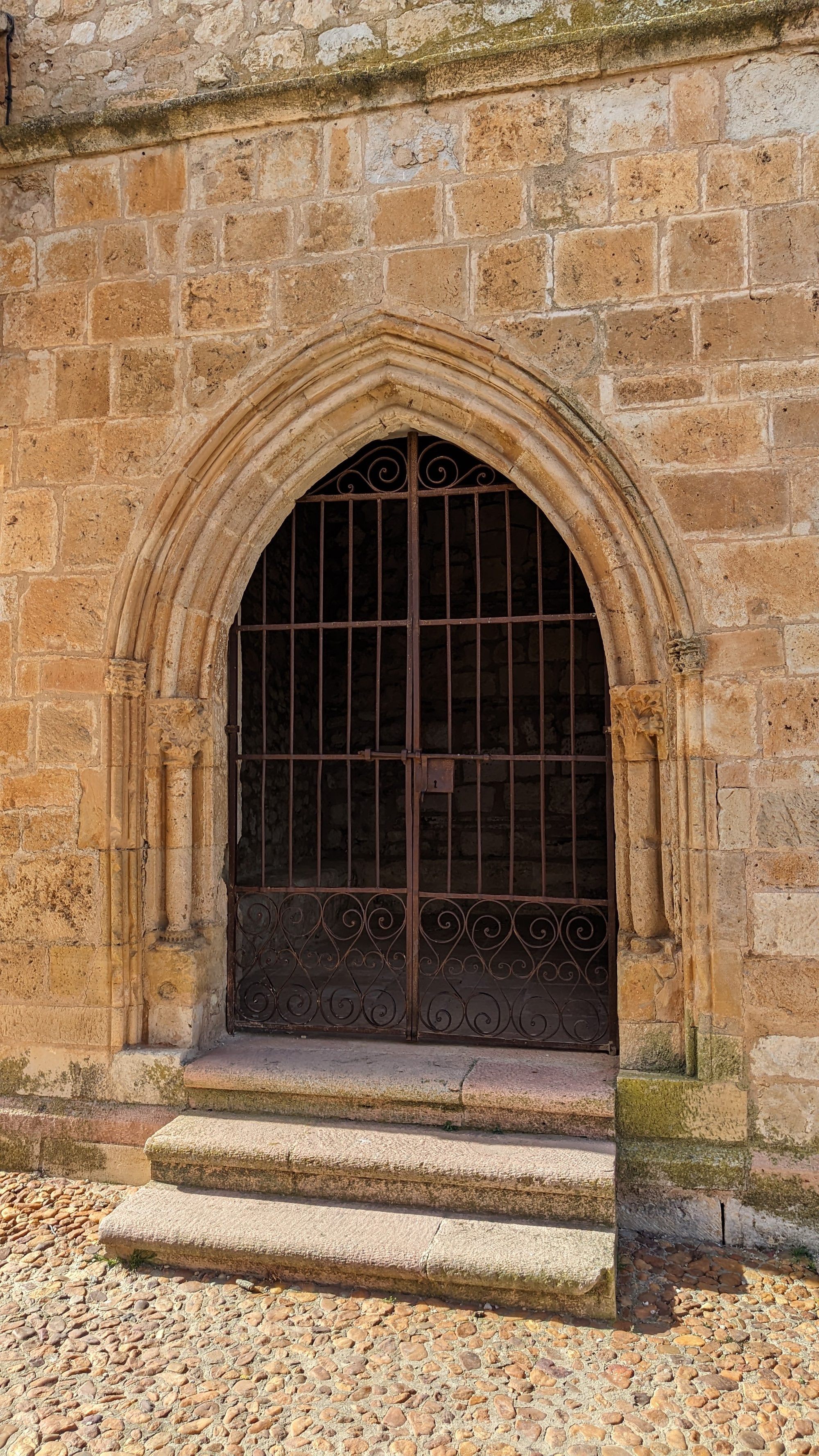 Puerta con arco ojival de piedra y reja de hierro forjado sobre escalones