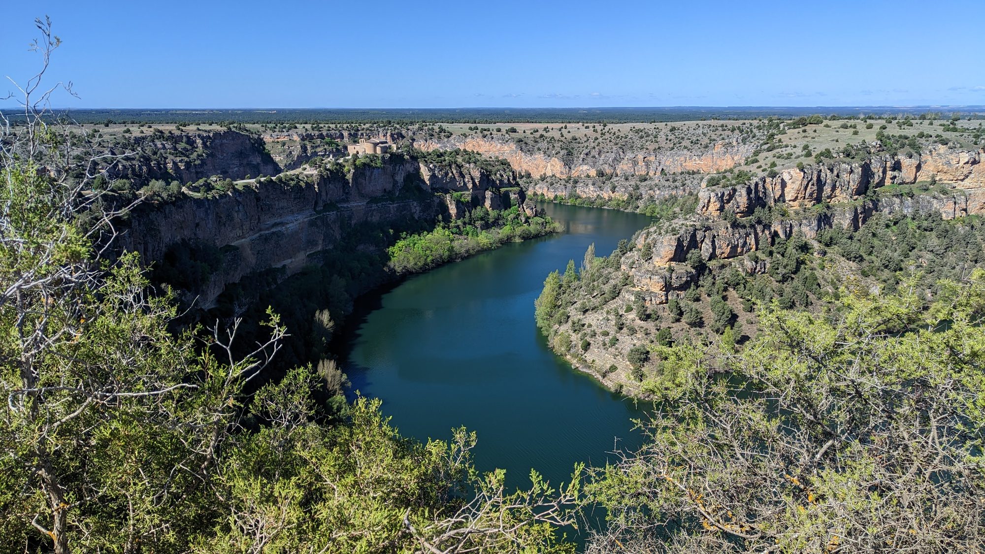 Gran meandro de río rodeado de acantilados rocosos y vegetación bajo cielo azul.
