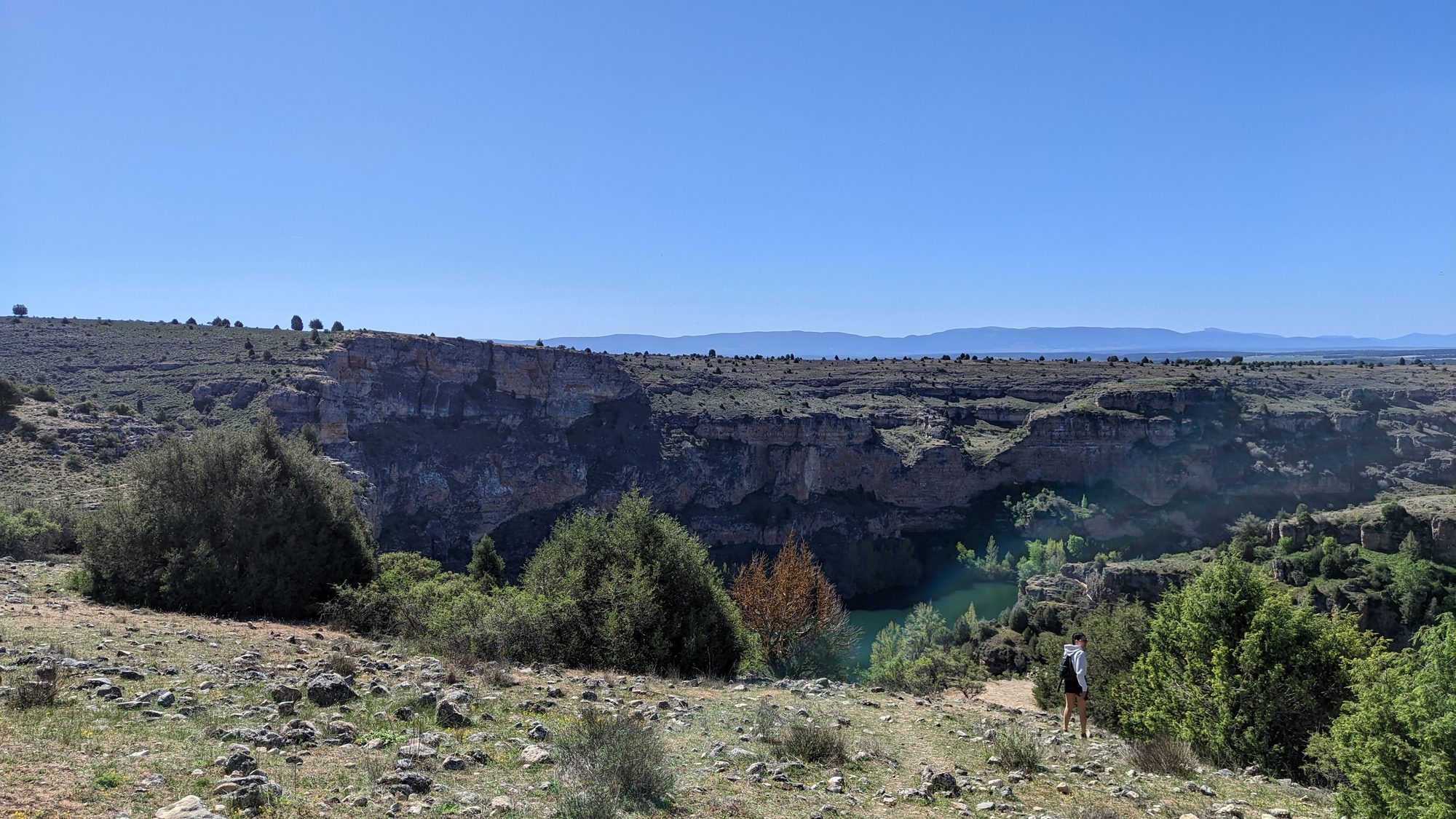 Cañón rocoso con río al fondo y vegetación mediterránea bajo un cielo azul despejado.