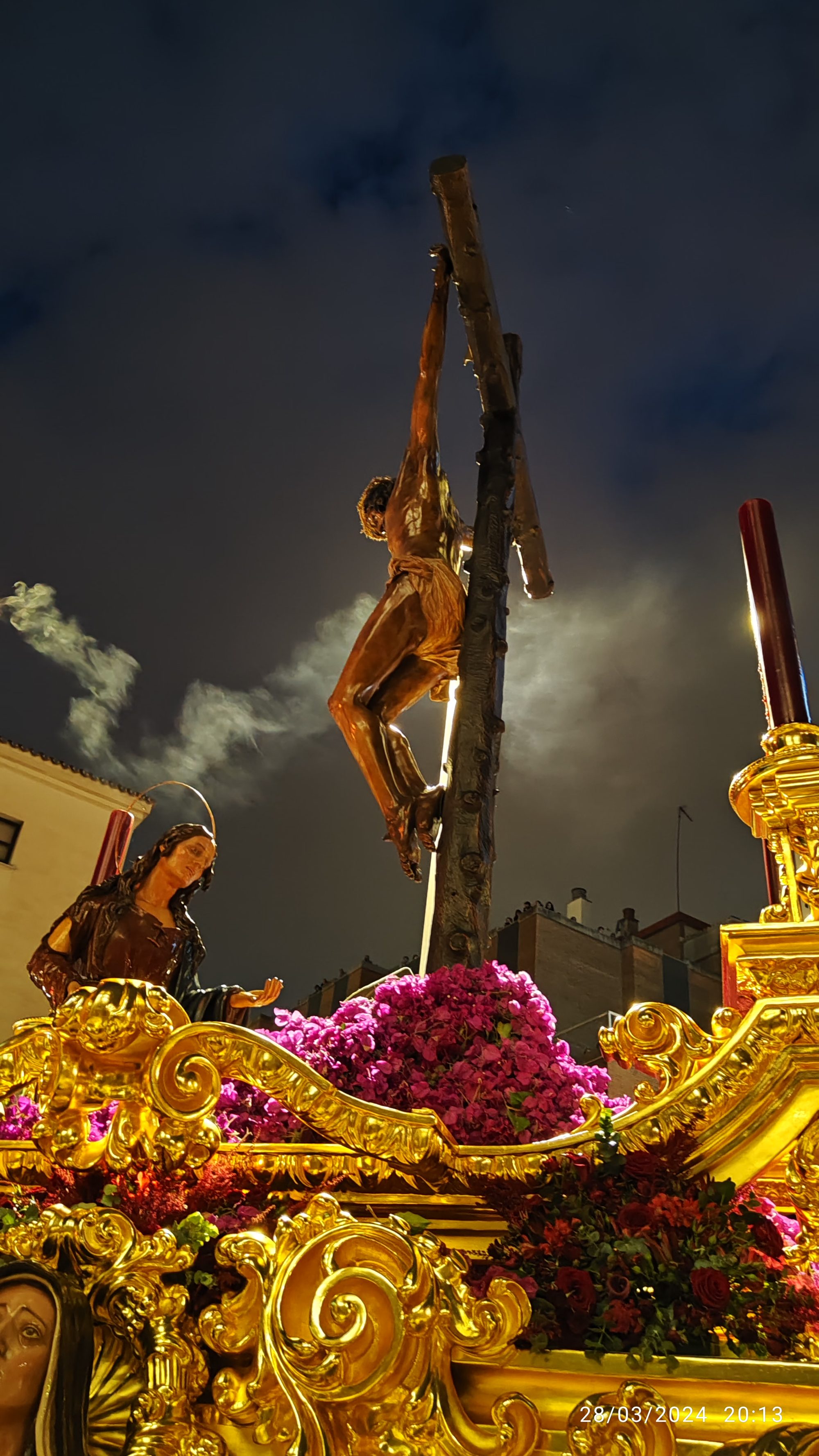 Cristo en la cruz sobre un trono procesional dorado e iluminado durante la noche.
