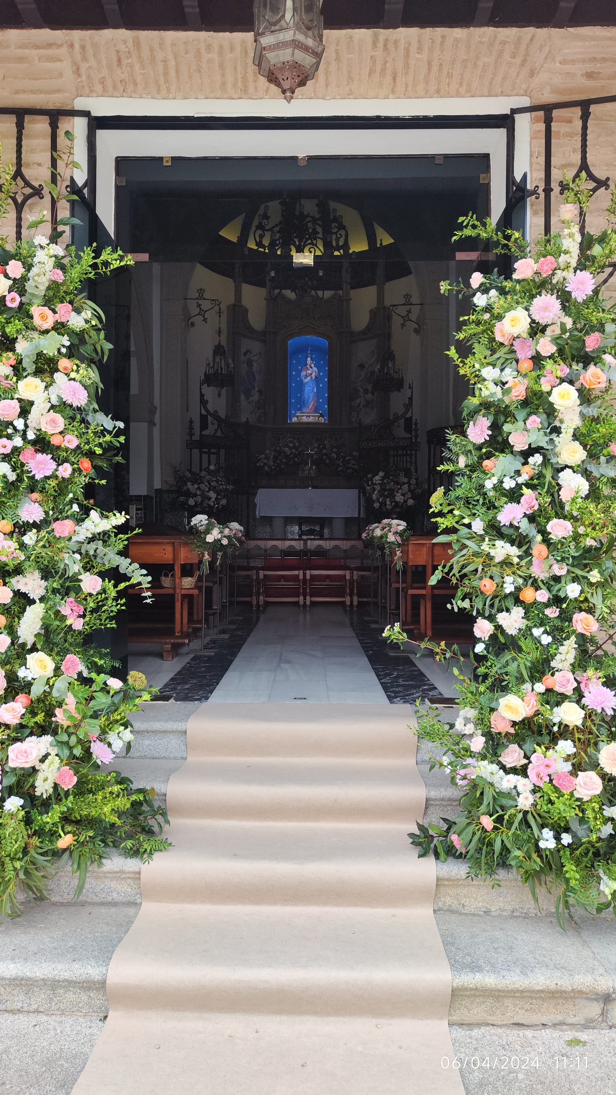 Entrada a una ermita en Toledo decorada con exuberantes arcos florales y alfombra.