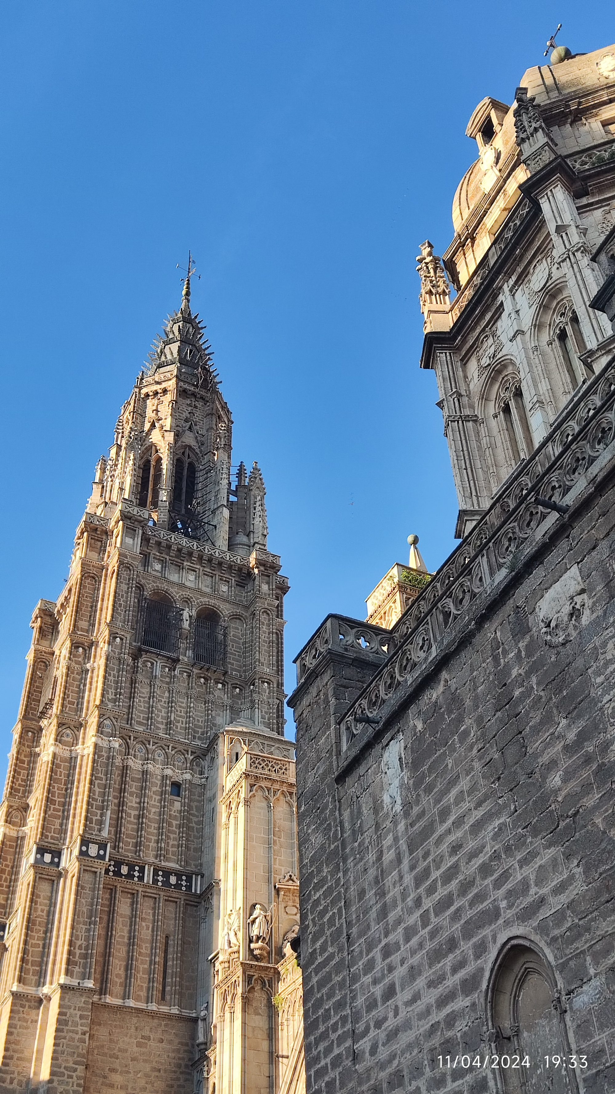Torre gótica y fachada de la Catedral de Toledo bajo un cielo azul despejado.