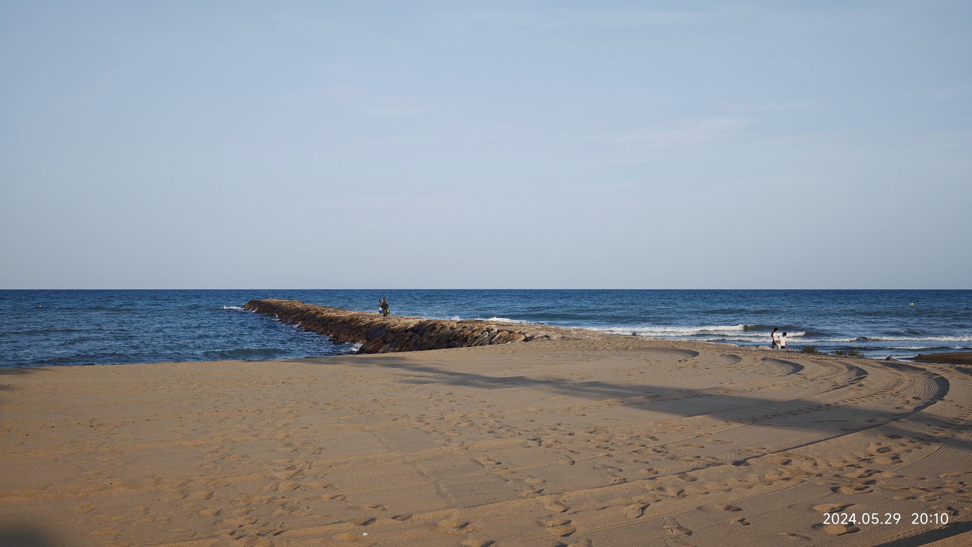 Escollera de rocas en la playa de arena junto al mar Mediterráneo azul.