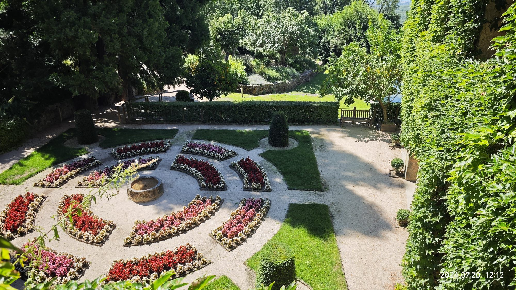 Jardín formal con parterres concéntricos de flores coloridas y fuente de piedra en Cuacos de Yuste.