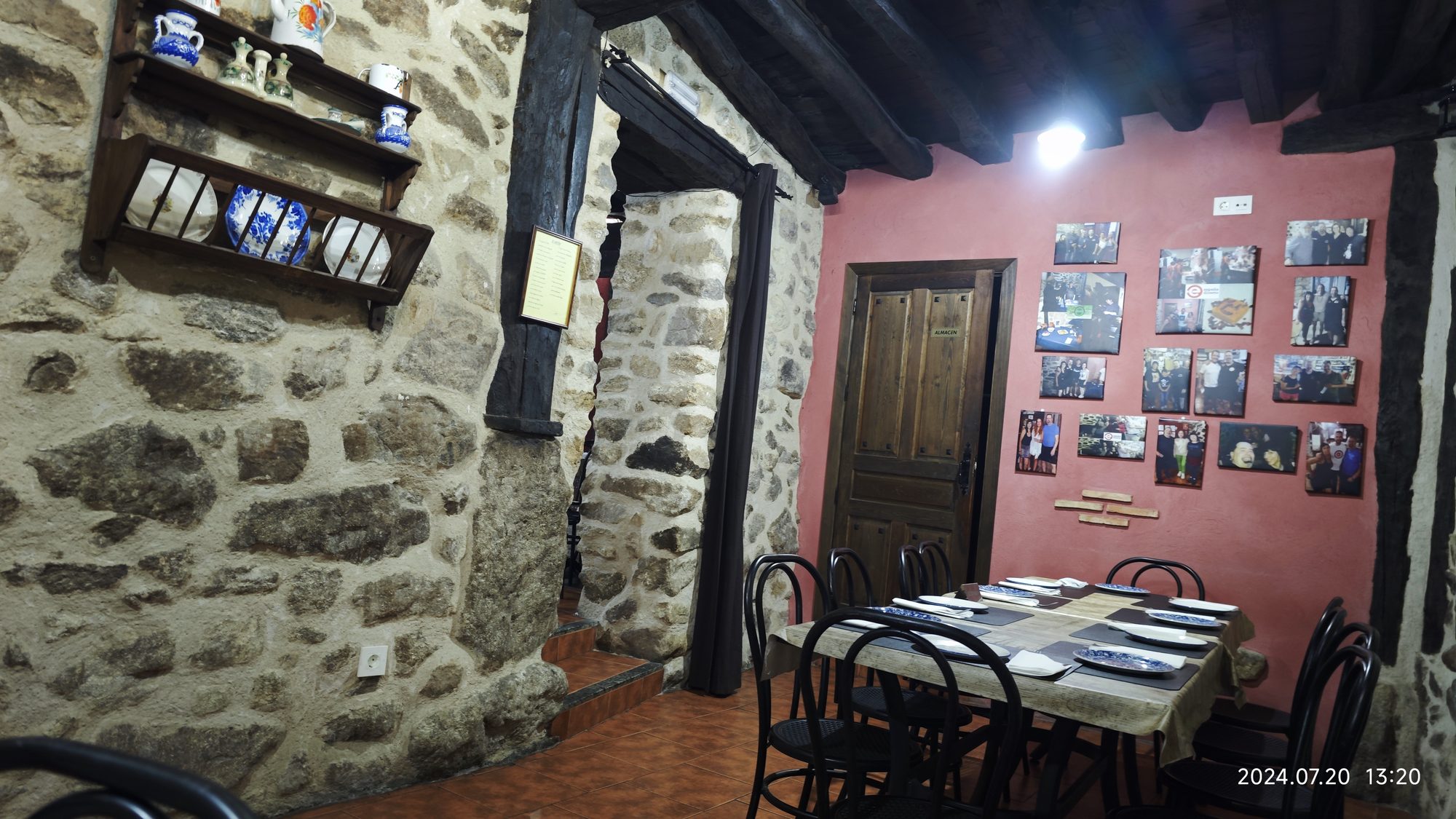 Comedor rústico con paredes de piedra, vigas de madera y mesa preparada para comer.
