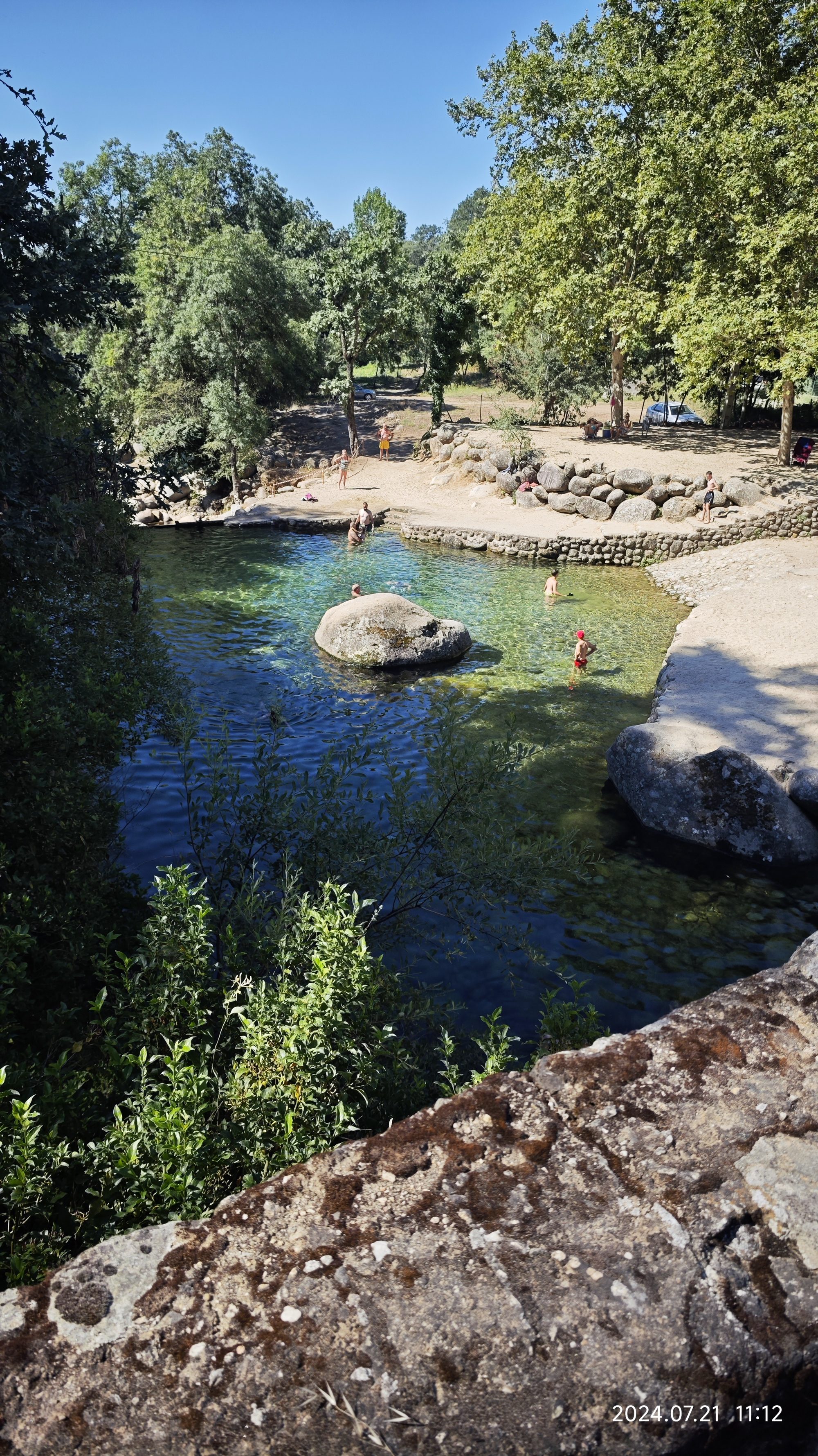 Piscina natural de aguas cristalinas rodeada de frondosa vegetación y grandes rocas.