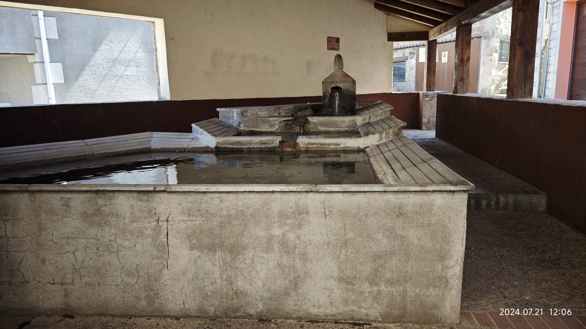 Lavadero tradicional de piedra con agua clara bajo una estructura con vigas de madera.