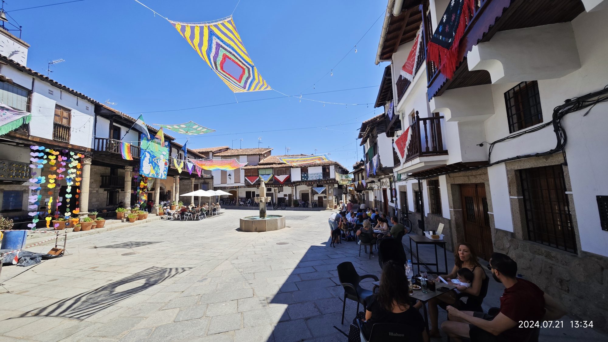 Plaza mayor de Valverde de la Vera con arquitectura tradicional y coloridos telares colgados.